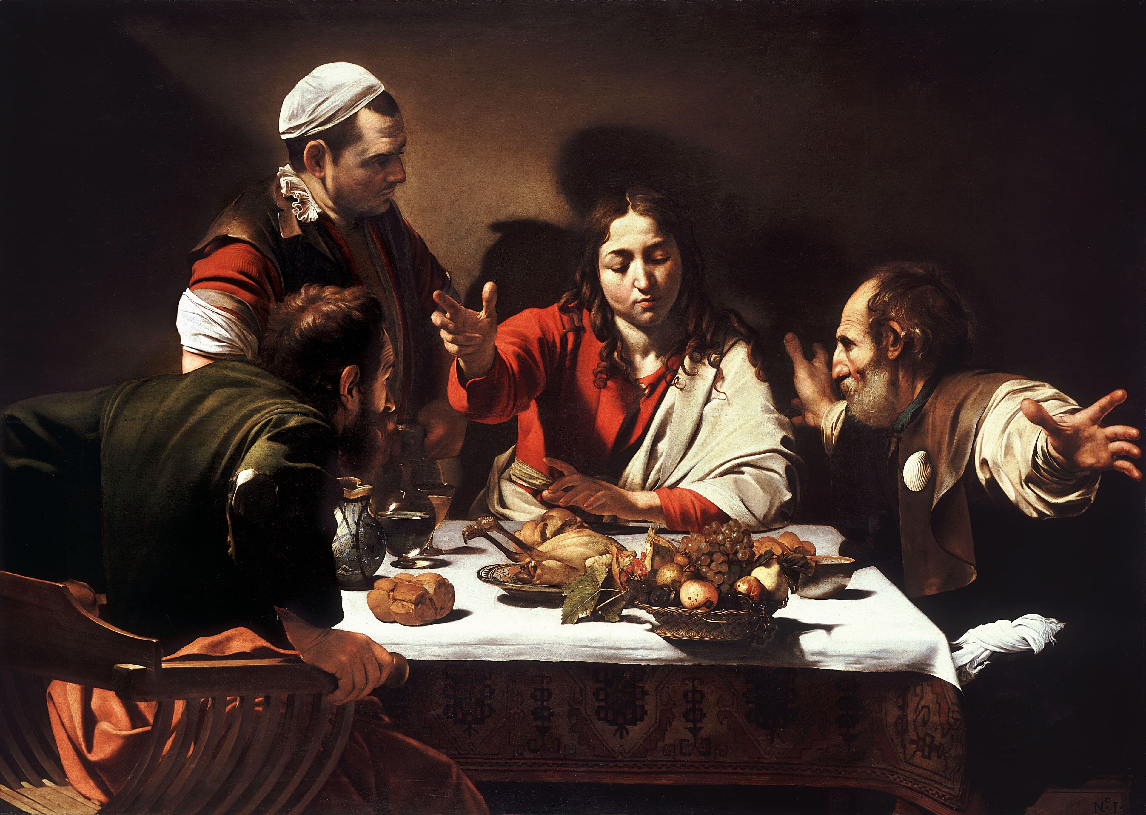 Four life-size figures around a table laid with a white cloth over a patterned carpet. At the centre a beardless Christ with long wavy hair, in a red tunic and cream mantle, raises his right hand open above the table. On the left a disciple in an olive-green jacket grips the arms of his chair as if to rise. On the right an older grey-bearded disciple in a brown jerkin with a white scallop shell pinned to his chest flings both arms wide. Behind them an innkeeper in a white cap stands and looks down, casting a large shadow on the bare wall. A wicker basket of grapes, pomegranate, pears and figs projects over the front edge of the table