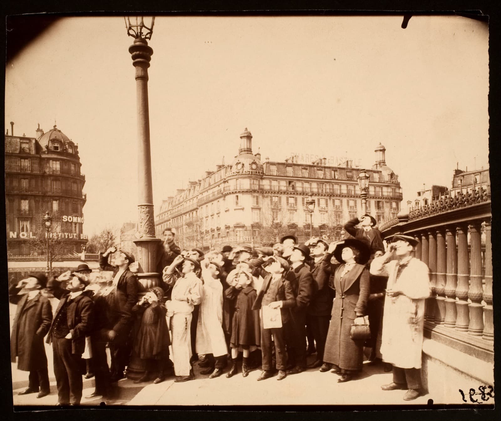 A dense crowd of men and women in hats and long coats standing in a public square, all with their heads tilted back and their faces turned up at the sky, several holding small dark panes of glass to their eyes