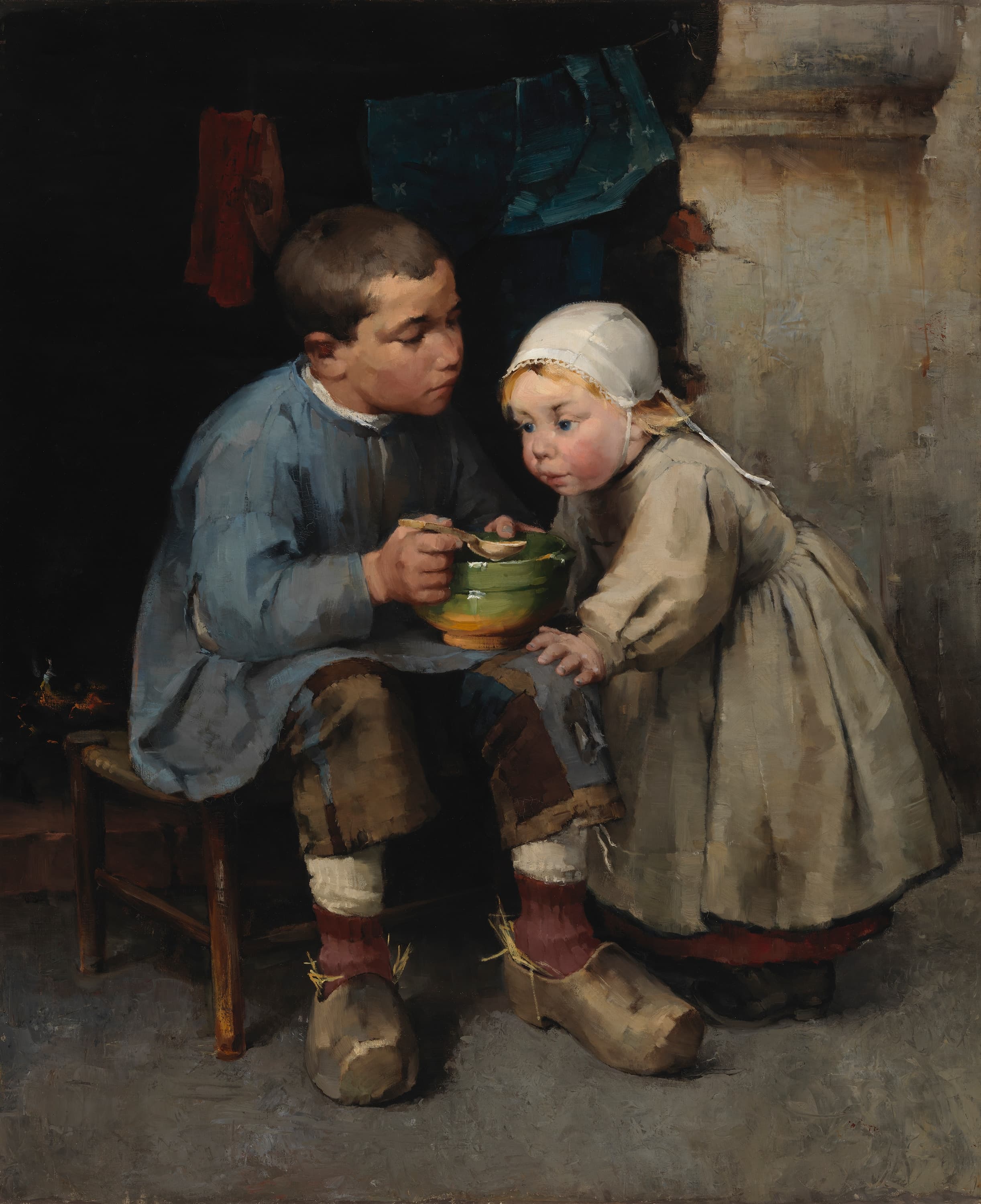 Helene Schjerfbeck's A Boy Feeding his Little Sister: a boy in a pale blue smock and patched brown trousers sits on a low wooden stool holding a green bowl and a wooden spoon, his straw-stuffed clogs on a gray floor, while a small girl in a white cap and a gray-beige dress with a red hem leans on his knee and watches the spoon, in a dark room with a fire at the left, a red garment and a blue printed cloth hanging above, and a pale plastered wall at the right