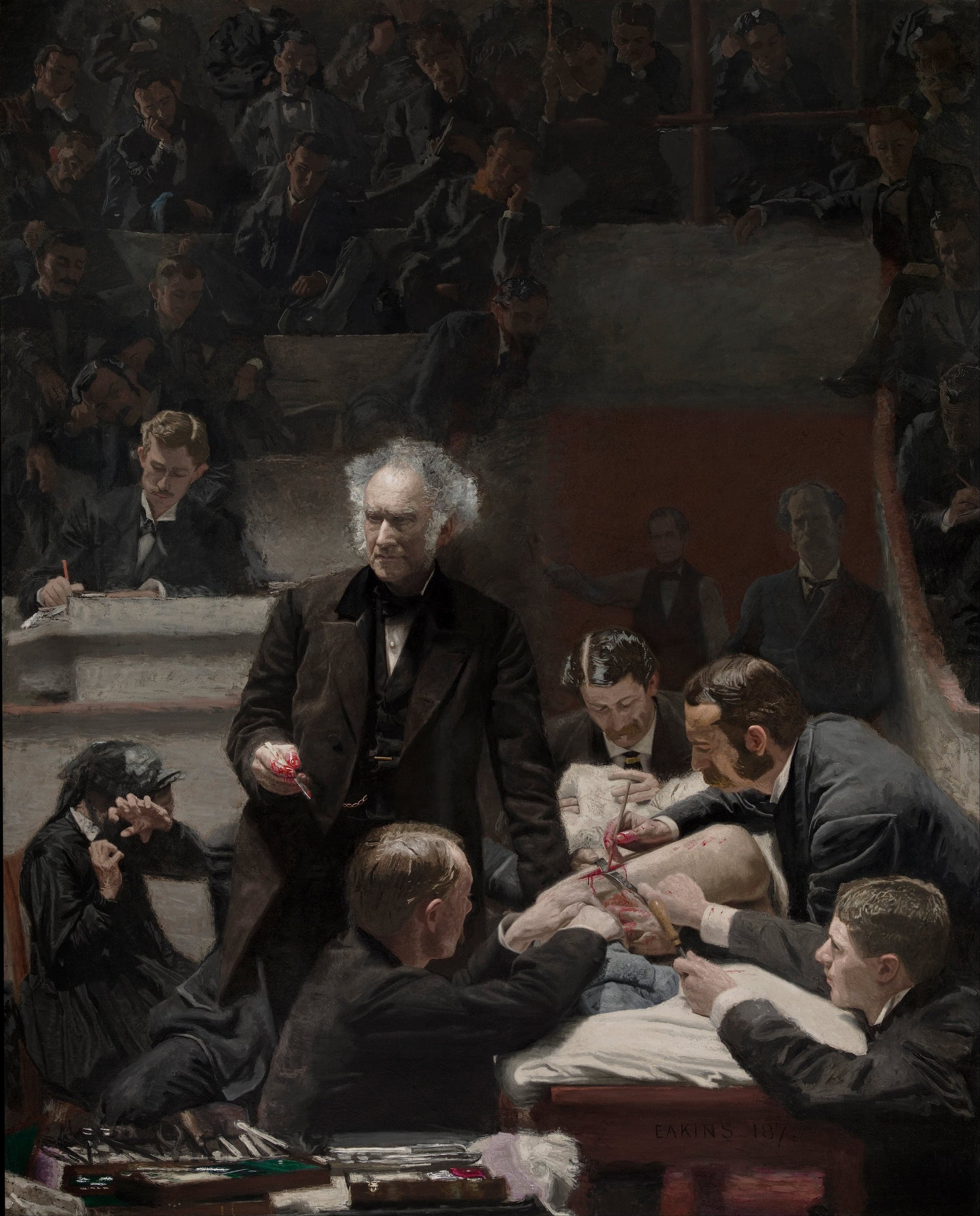 A tall dark painting of a surgical amphitheatre. A white-haired surgeon in a black frock coat stands at the centre holding a bloodied scalpel in his right hand and looking up towards the viewer's left. Four doctors in dark coats bend over a patient on a table at the right, one holding a folded white cloth over the patient's face, two working at an open incision on the thigh, one holding the grey-stockinged legs. At the lower left a woman in black hides her eyes with a clawed hand. A clerk writes at a desk behind, two men stand in a red-brown tunnel doorway, and rows of students sit in near darkness above. The words EAKINS 1875 are on the front of the table.