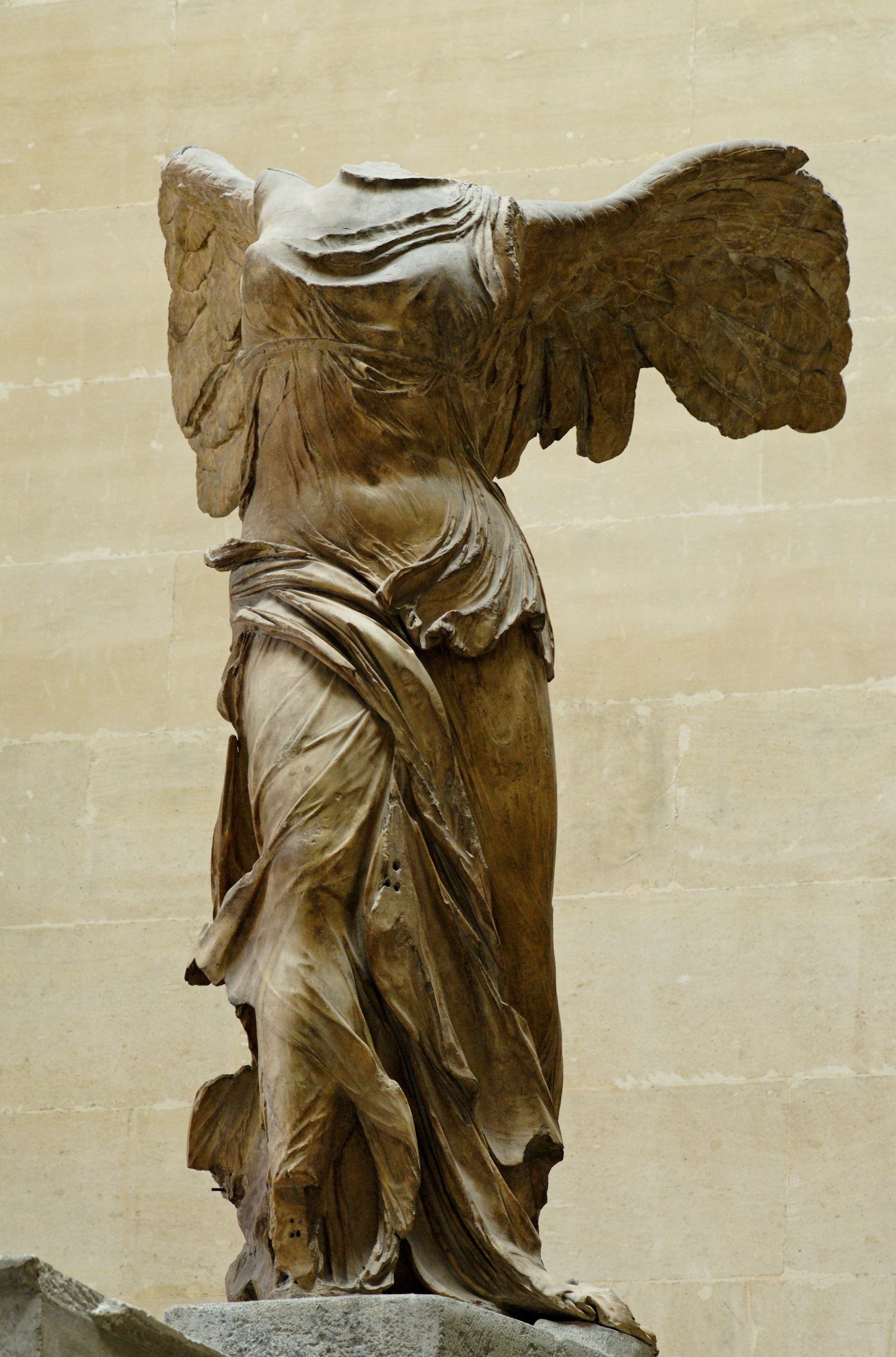 The Winged Victory of Samothrace in the Louvre: the headless marble goddess Nike leaning forward with both wings spread and windblown drapery pressed against her body