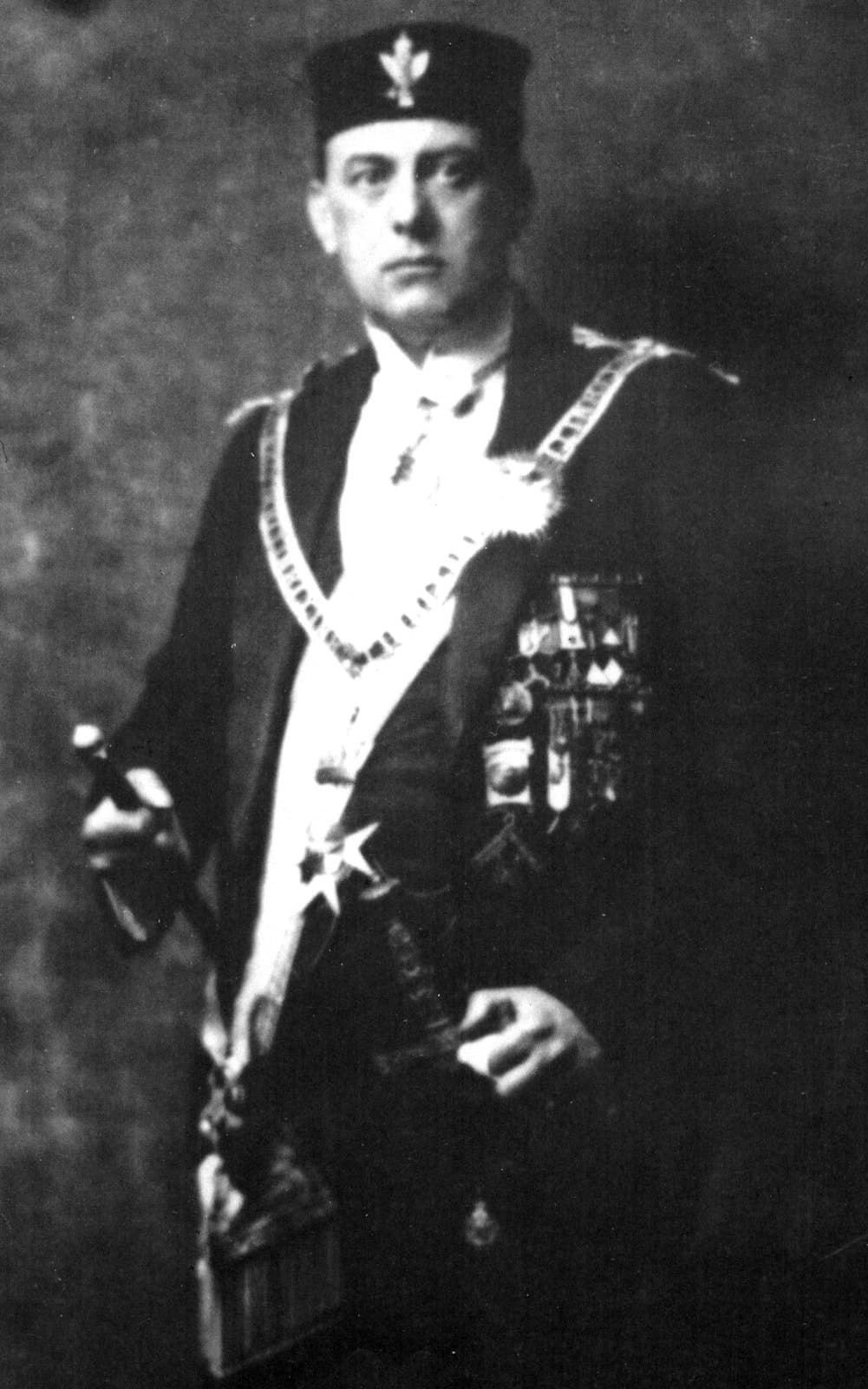 Aleister Crowley seated in ceremonial O.T.O. robes, sash, medals, and cap