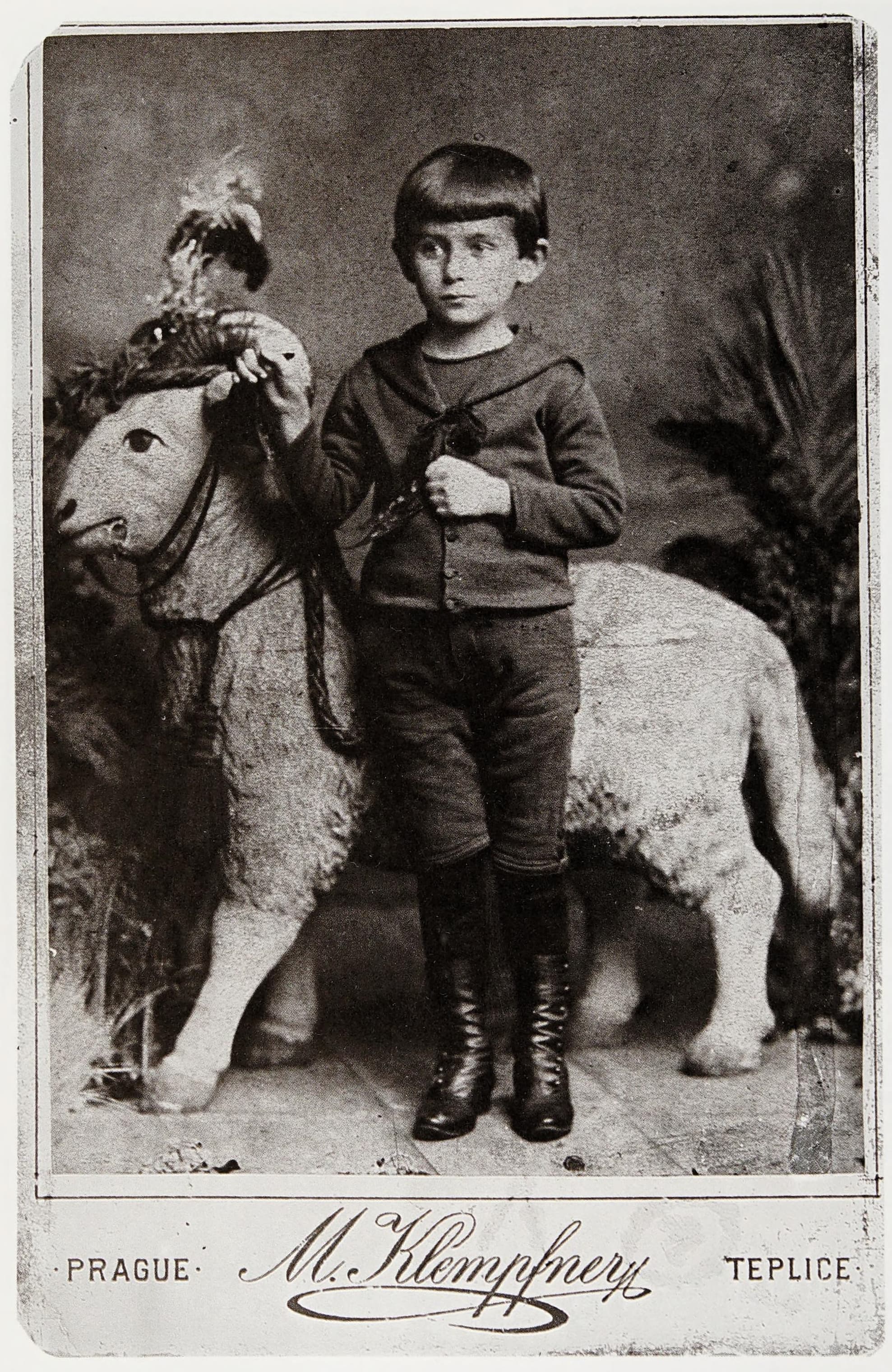 Studio photograph of Franz Kafka as a boy of about five, standing in a buttoned coat with a walking cane, looking directly at the camera.