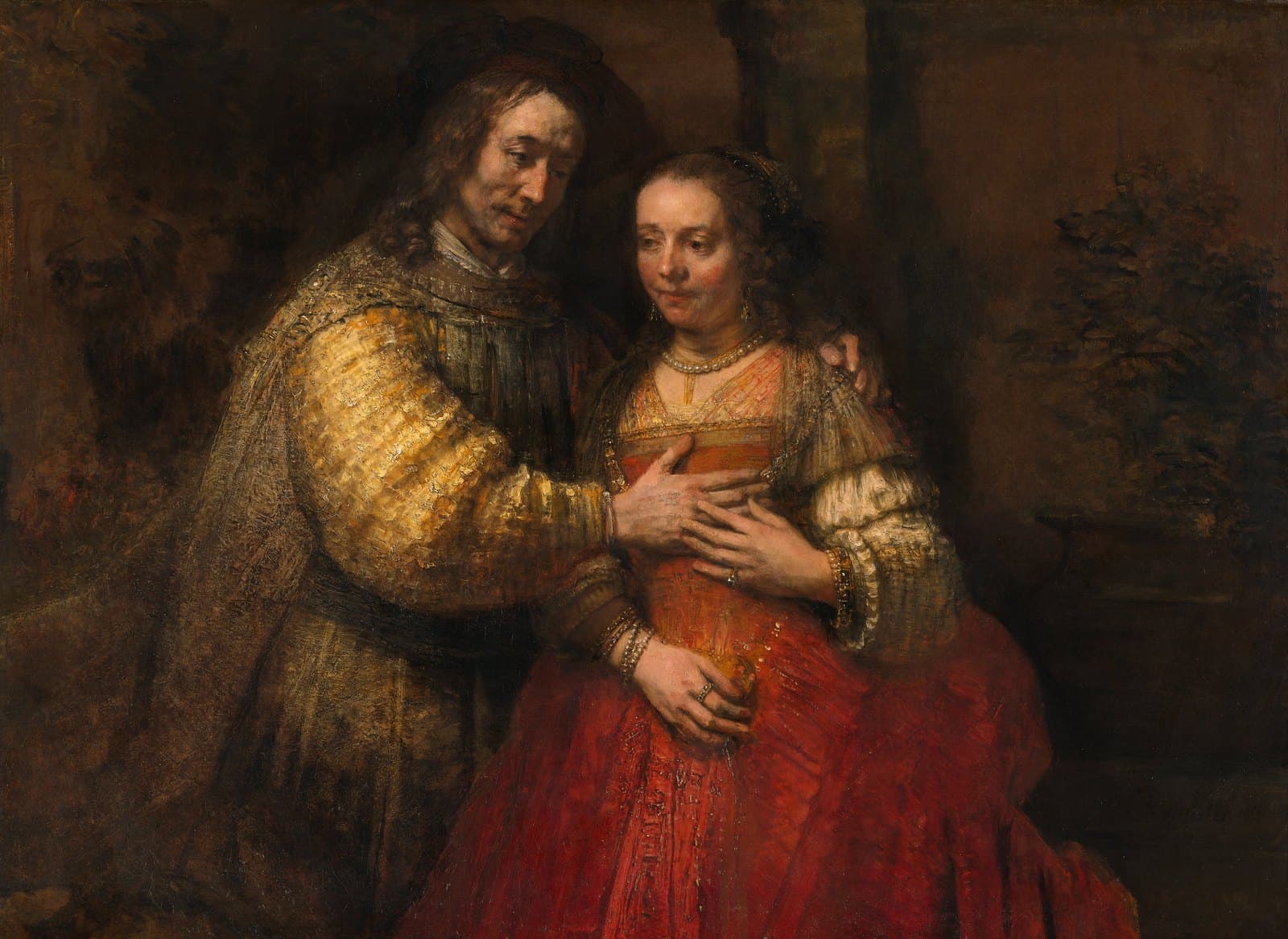A man and a woman stand close together against a dark brown background. The man, in a gold sleeve and a dark cloak, rests his right hand on the woman's chest and his left on her shoulder. The woman, in a red dress with a pearl necklace and bracelets, lays her hand over his. Both look down rather than at each other.