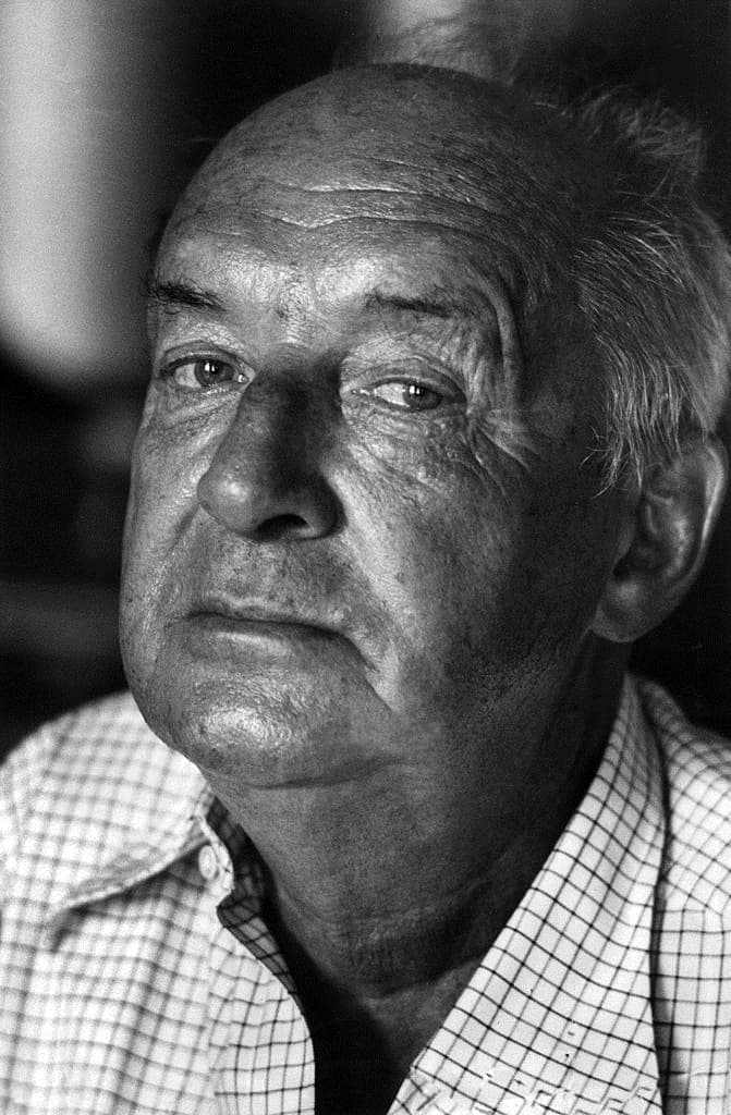 Black-and-white portrait of Vladimir Nabokov in his seventies, in a dark jacket, chin resting on his hand, eyes narrowed in thought