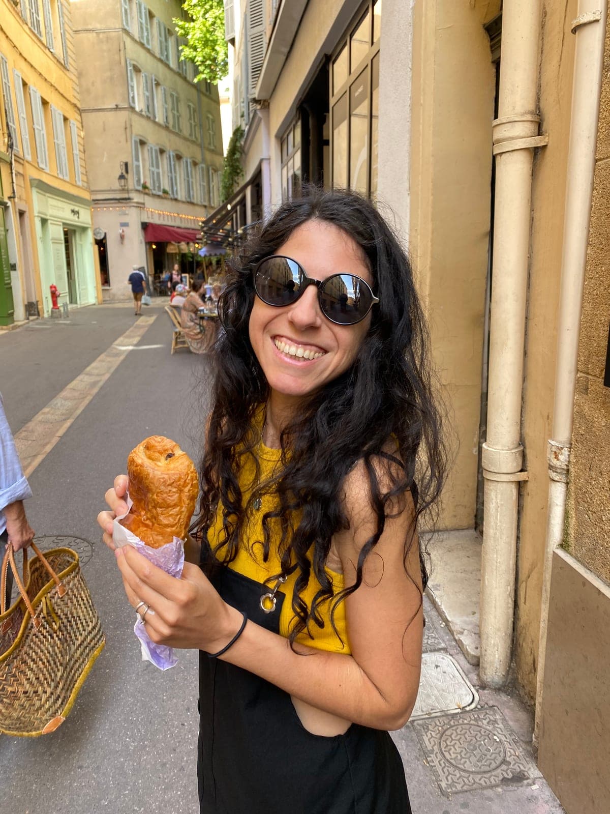 Adriana smiling with a pain au chocolat in a narrow street in Aix-en-Provence