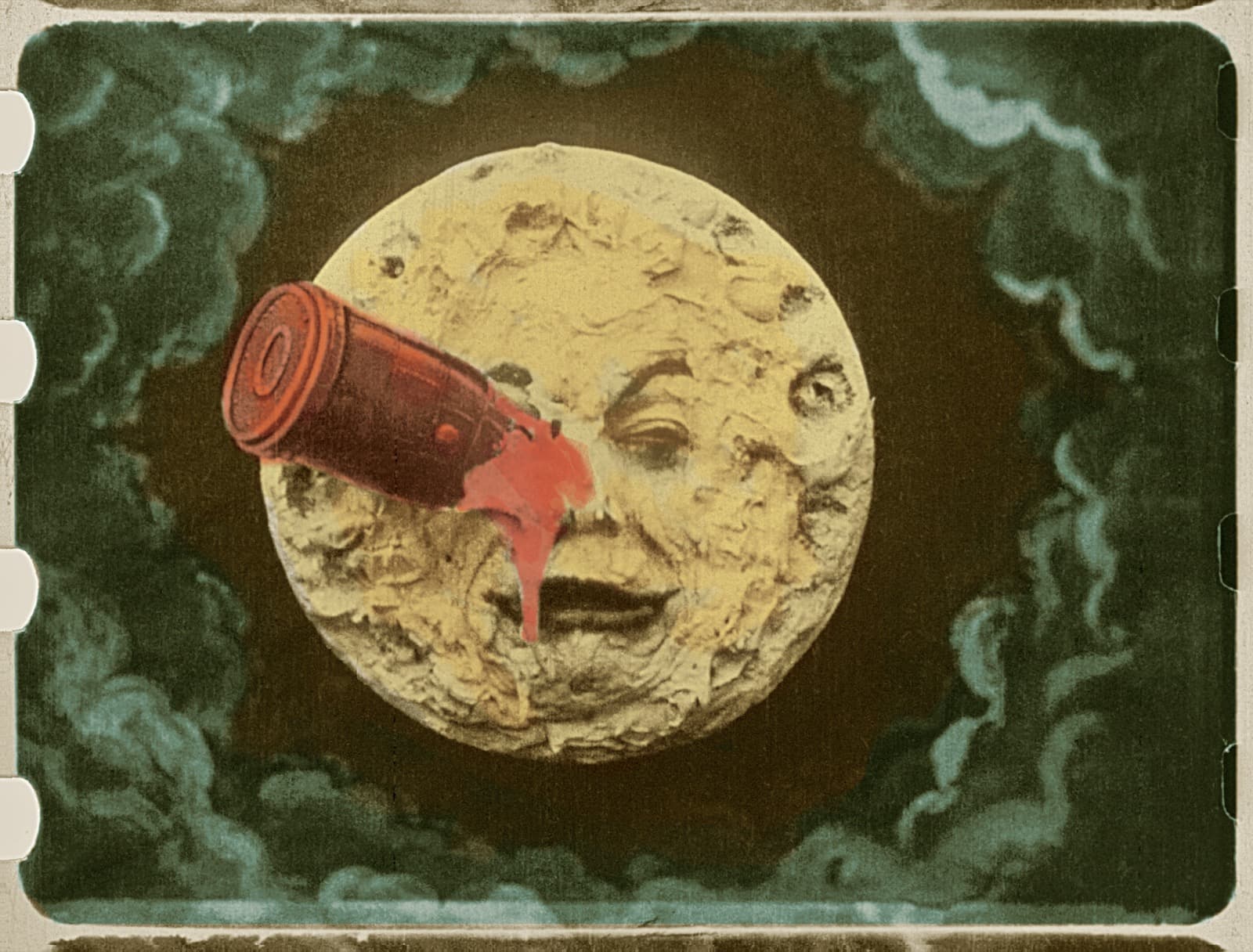 Hand-colored frame from A Trip to the Moon: the Man in the Moon's cratered face against teal clouds, a red bullet-shaped capsule lodged in his right eye