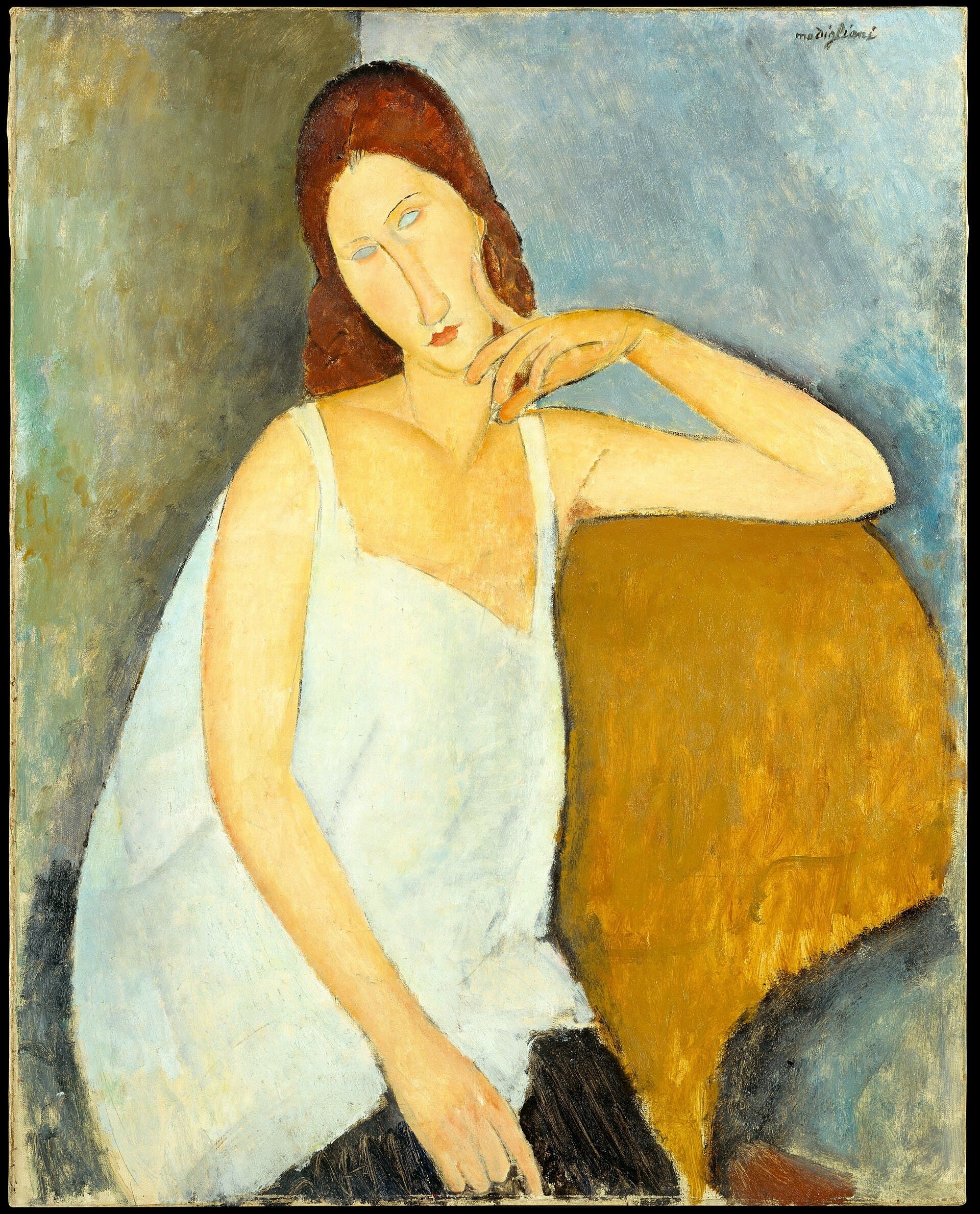 A woman with long auburn hair and pale blank eyes sits in a large ochre-yellow armchair, her head tilted to the right and her chin resting on the curled fingers of her left hand, her left arm laid along the chair back. She wears a white chemise with thin straps, and her right arm hangs straight down to a dark skirt. The wall behind her is olive brown on the left and pale blue on the right. Signed modigliani at upper right