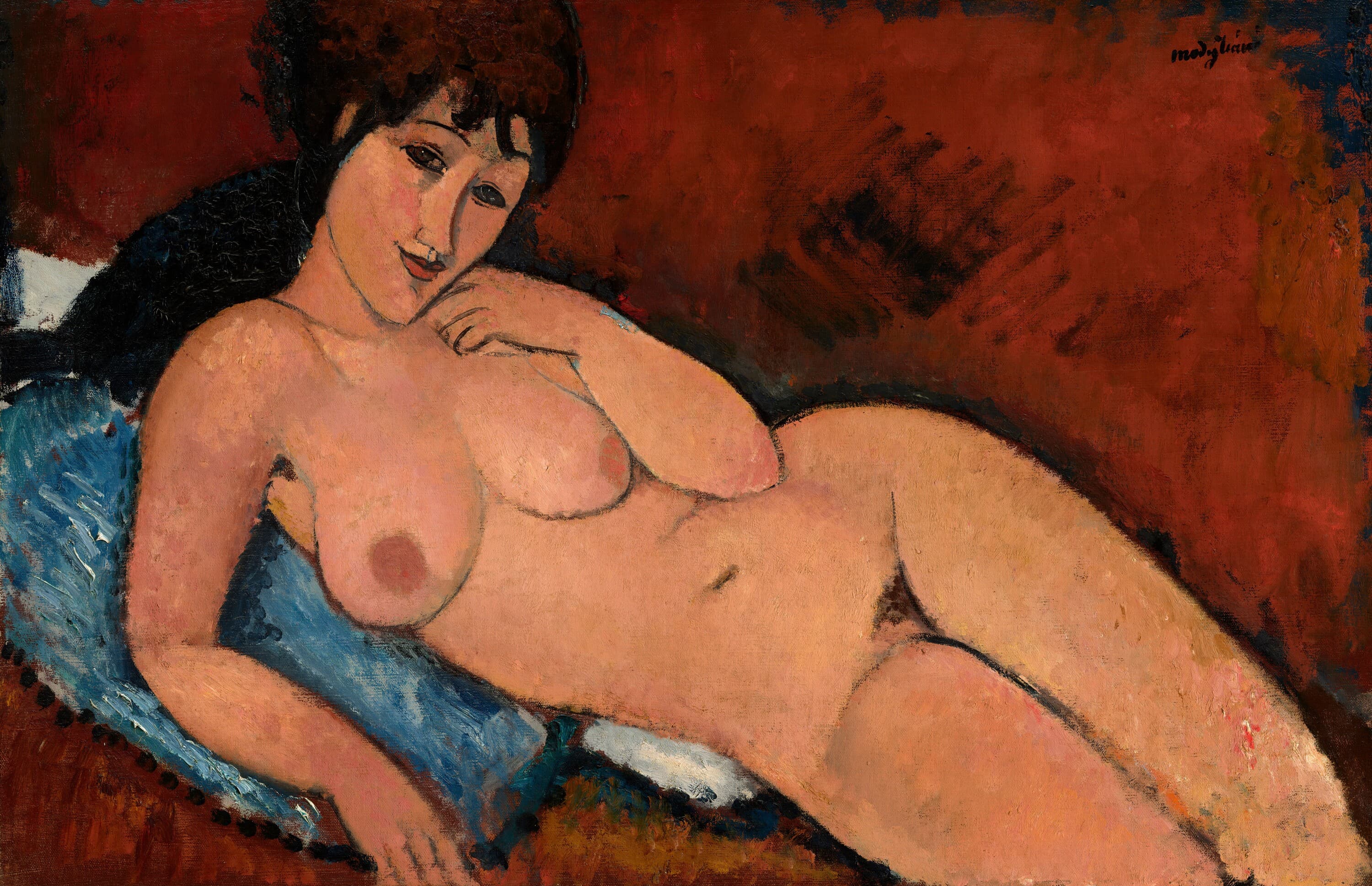 A nude woman with dark hair and bangs reclines across the canvas on a blue cushion, her body facing us and her face resting on the back of her left hand, propped on her right elbow. Her legs run off the right edge. The background is a warm red-brown, a white cloth shows under the cushion, and a row of dark dots runs along the lower left. Signed modigliani at upper right