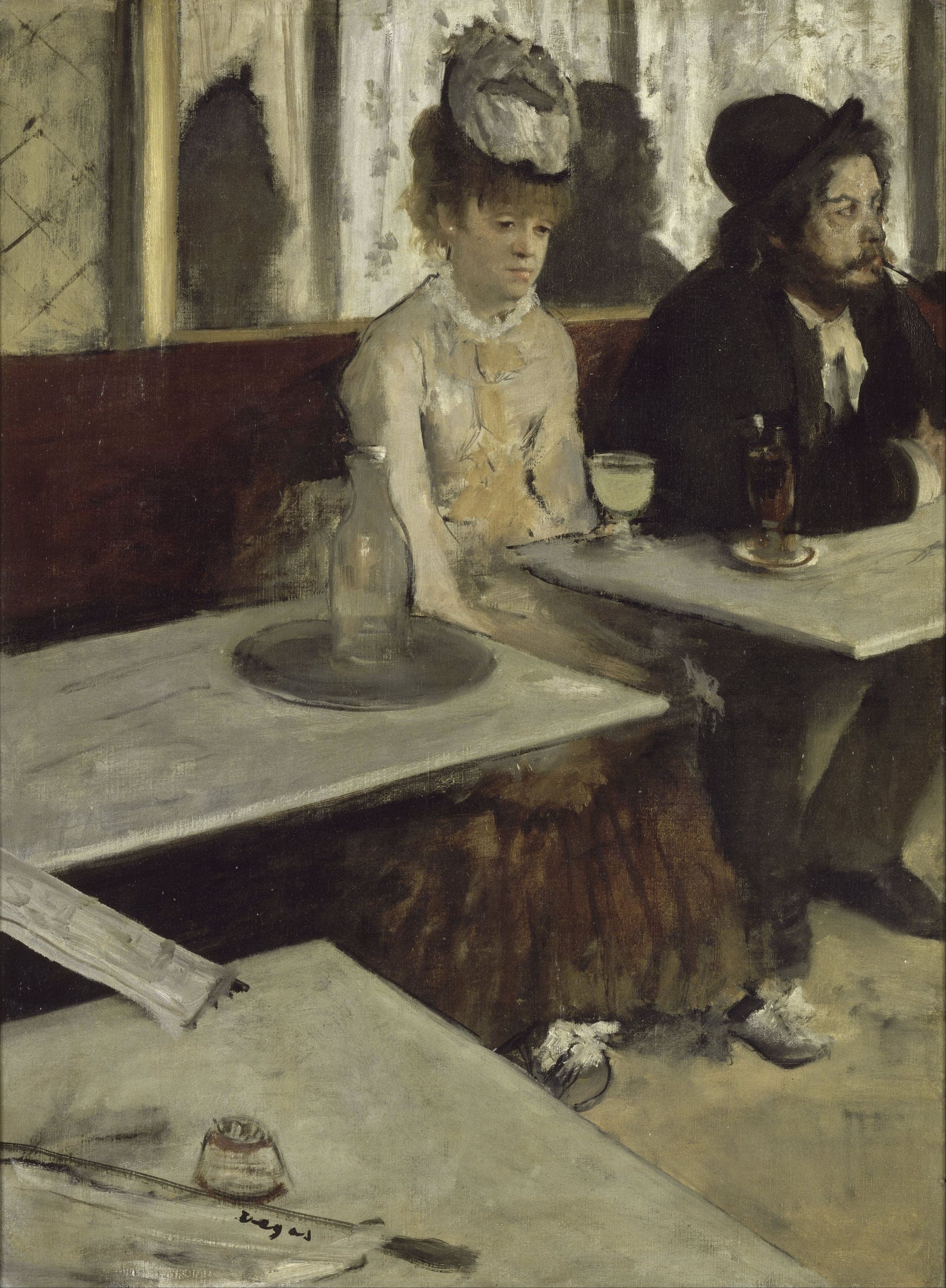 A woman in a pale dress and a small gray hat sits on a café banquette staring downward, a tall glass of cloudy pale-green liquid on the marble table in front of her. A bearded man in a black hat sits to her right with a pipe in his mouth, looking away out of the picture. Two more marble tabletops run diagonally into the foreground. The far one holds a glass carafe on a tray, with the woman's hand resting on its edge; the near one holds a small match stand. A folded newspaper on a wooden rod bridges the gap between them at the lower left. A mirror behind them reflects two dark silhouettes.