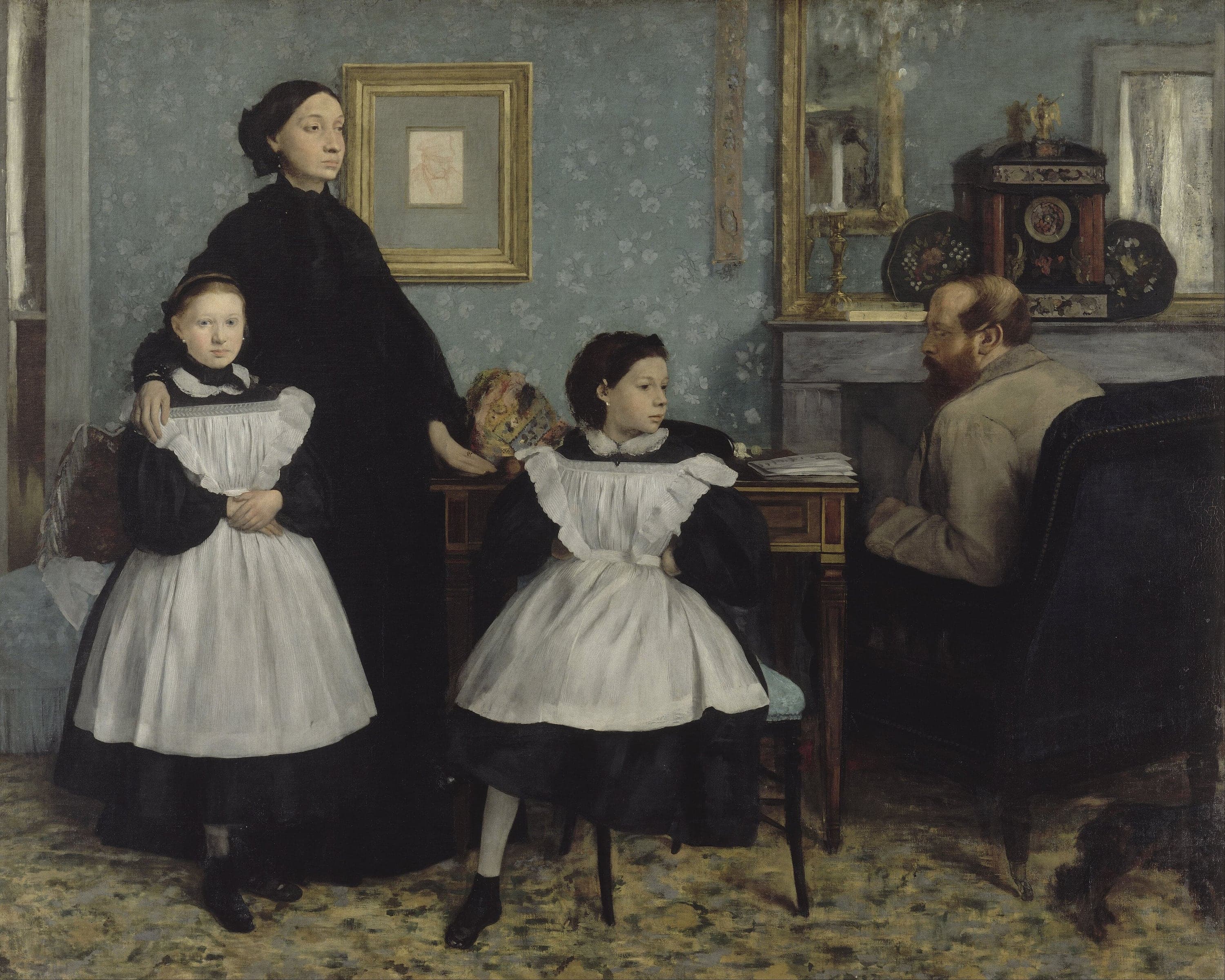 A wide interior with pale blue wallpaper patterned with small white flowers. A woman in a full black mourning dress stands at the left, her right hand on the shoulder of a girl in a black dress and white pinafore. A second girl in the same black-and-white clothes sits on a chair in the center with one leg drawn up. At the right a bearded man in a gray jacket sits in a dark armchair beside a marble fireplace, turning his head toward the others. A framed red-chalk drawing hangs on the wall and a mirror hangs above the mantelpiece; a dog's hindquarters are cut off by the lower right corner.