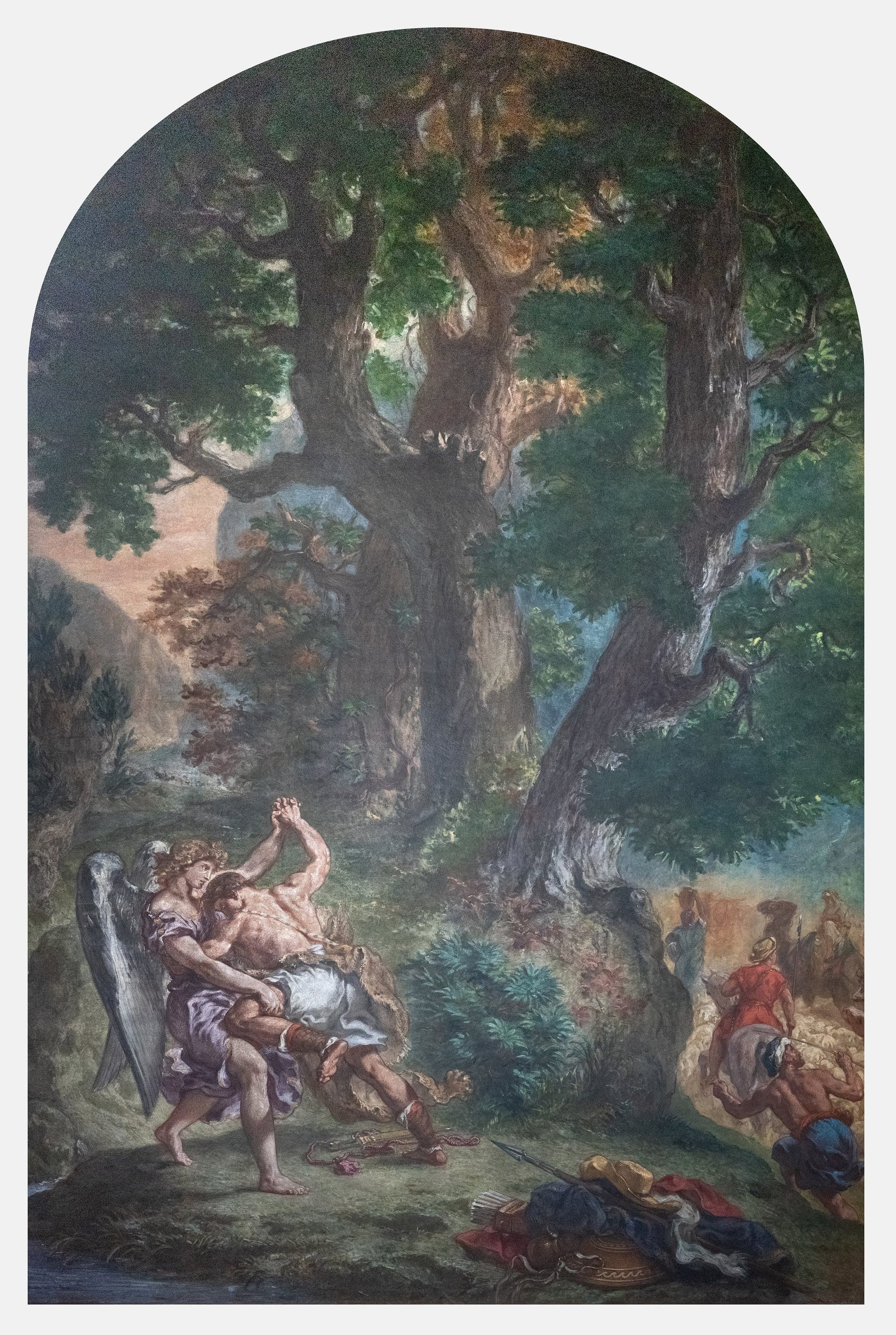 A tall arched wall painting. At the lower left a bare-chested man locks arms overhead with a winged figure in a lilac robe, his foot braced in the grass. A quiver of arrows, a spear, a wide yellow hat, red and blue cloaks and a gold bowl lie heaped in the foreground. Huge oaks fill the upper two-thirds and close off the sky, and at the right edge small figures drive sheep and pack animals along a track into a pale valley