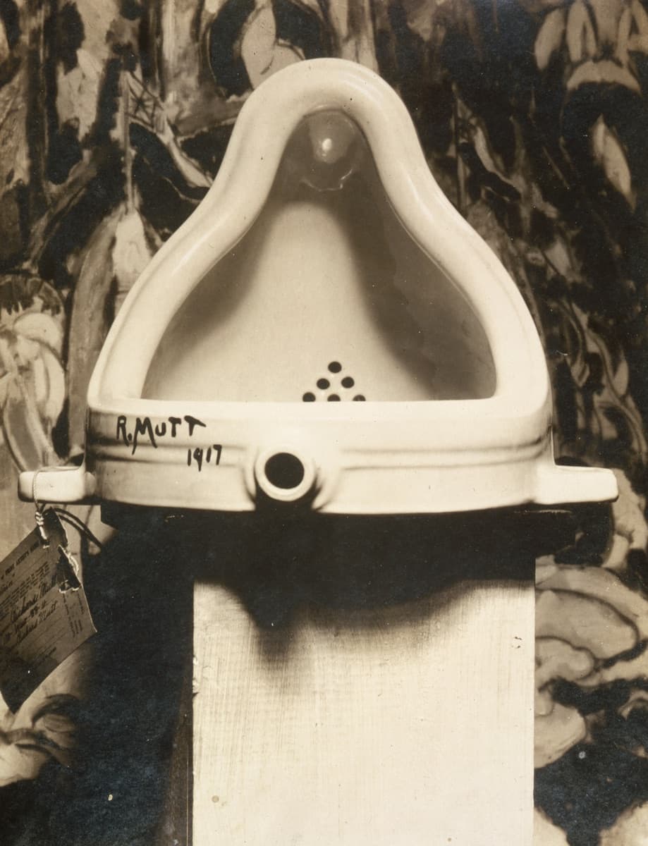 Alfred Stieglitz's 1917 photograph of Fountain: a white porcelain urinal laid on its back on a wooden pedestal, signed "R. Mutt 1917", an entry tag hanging from it, against a painted backdrop.
