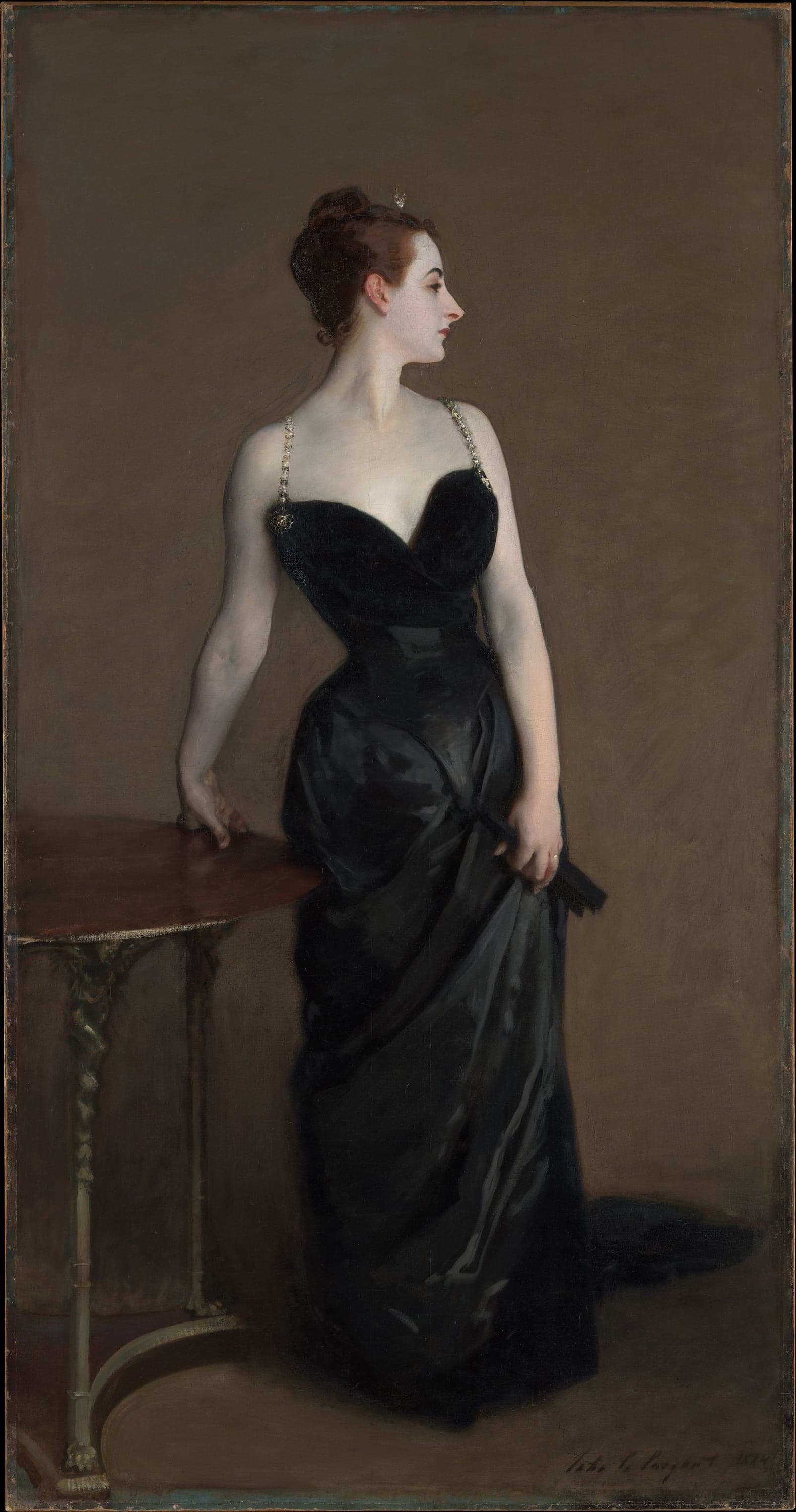 A woman in a sleeveless black evening dress with thin jeweled straps stands turned in profile to the right against a plain brown-gray wall, her skin painted a pale lavender-white; her right hand presses on the mahogany top of a small gilt-legged table and her left hand holds a closed black fan against the dark skirt.