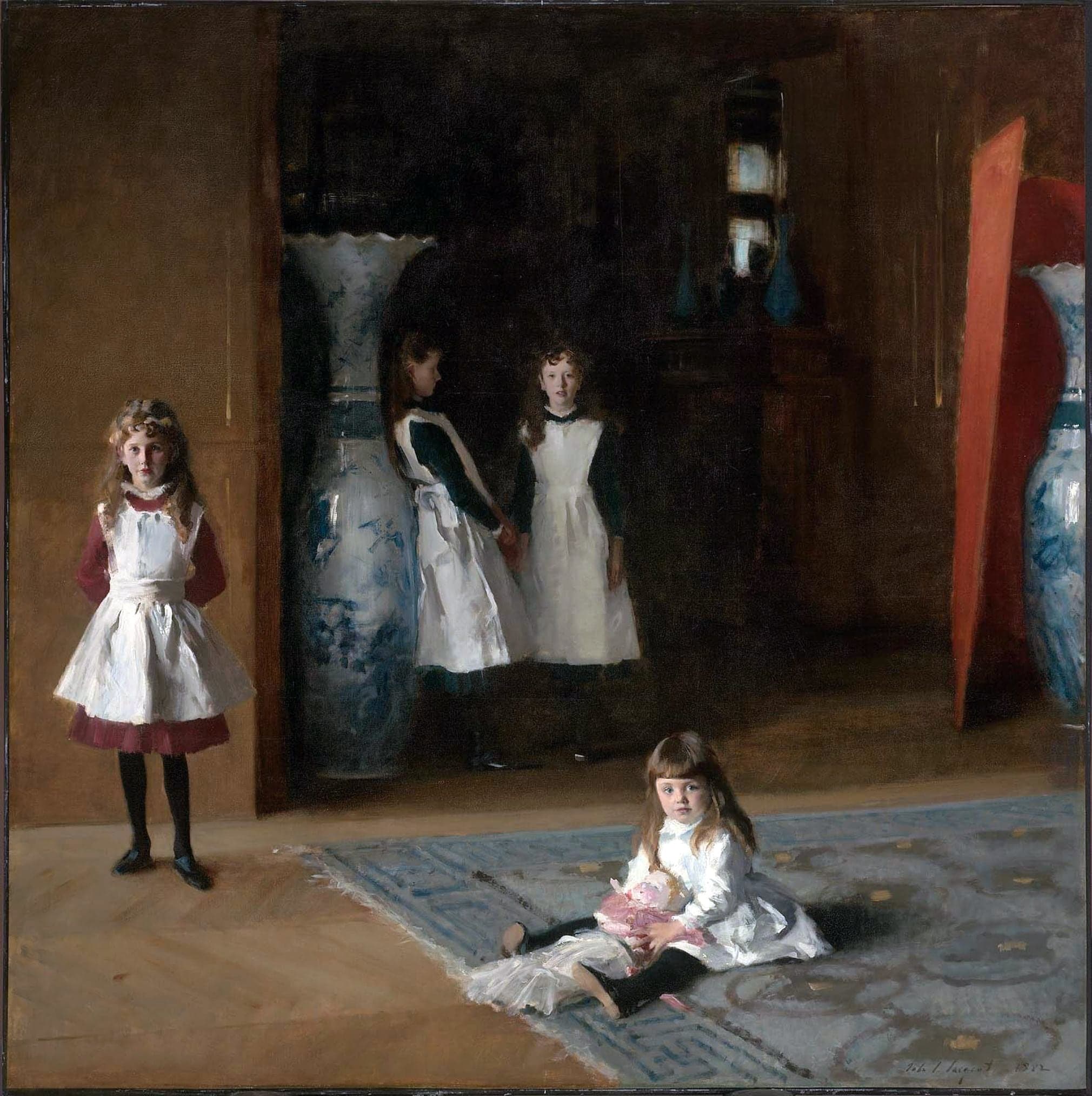 Four girls in a dim, nearly square room: the youngest sits on a patterned rug in the foreground holding a doll, one stands alone at the left in a white pinafore over a red dress, and two more stand in shadow further back, flanked by two tall blue-and-white Japanese vases, with a red panel at the right edge.