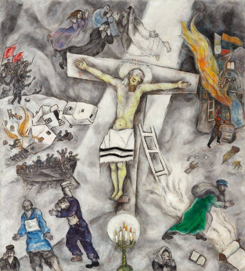 Christ hangs on an upright cross at the centre of a grey canvas, his head wrapped in white cloth under a pale halo and a fringed white prayer shawl with two black stripes tied round his hips. A broad shaft of white light runs down the canvas behind him and a plain white ladder leans against the cross. Four figures float above the crossbar, three bearded men in dark coats and a woman in purple. On the left a village of white houses lies overturned with one alight, soldiers come down a slope under three red flags, and an open boat rides low with crowded passengers. On the right a synagogue burns beside its open ark and the tablets of the Law, and a man in a green coat runs off with a white bundle. A brass candelabrum with lit candles stands in a circle of white at the bottom