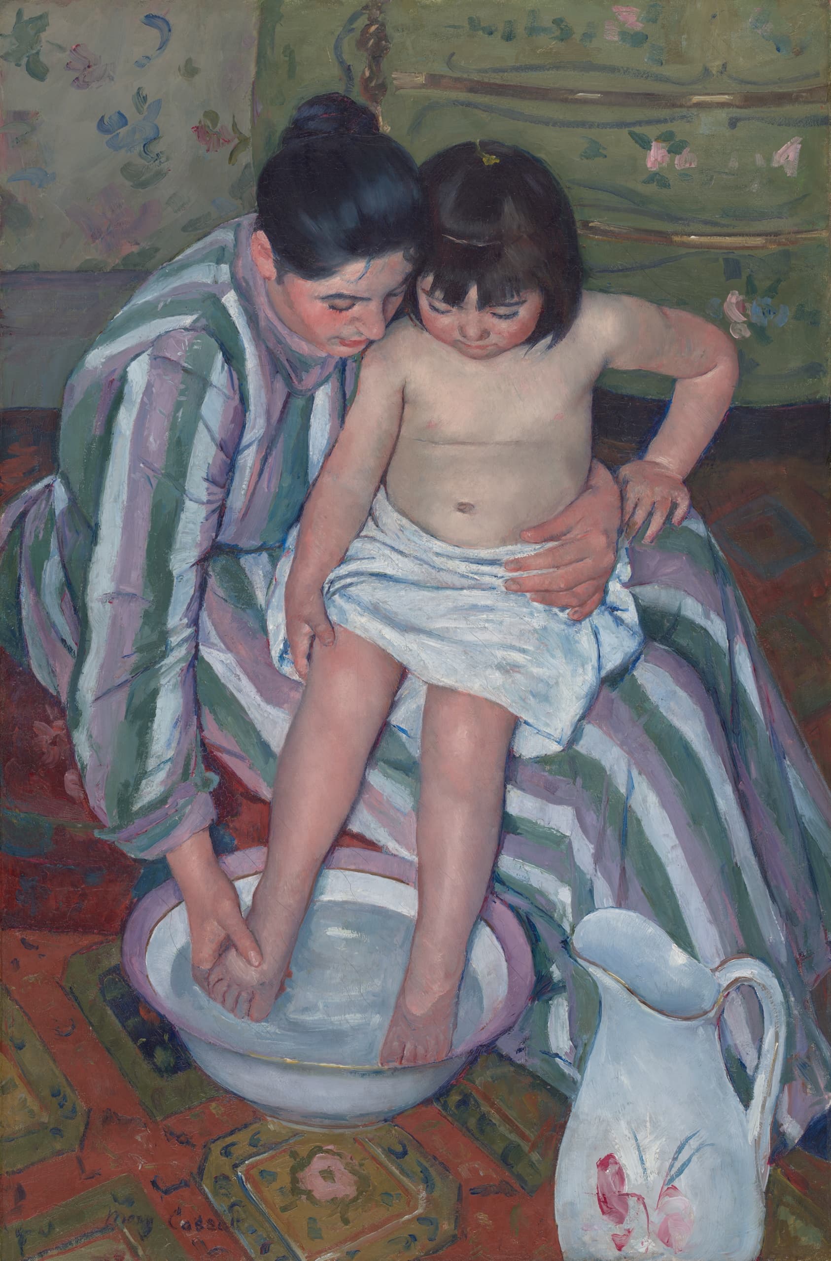 Seen from above, a woman in a mauve-and-white striped dress holds a child wrapped in white on her lap and washes the child's foot in a flowered basin, a decorated pitcher beside them on a patterned red carpet