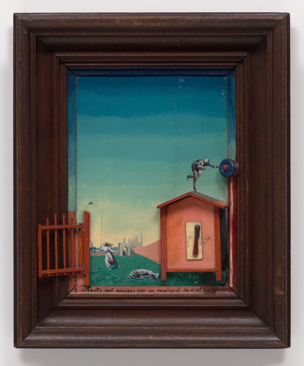 A painted landscape inside a deep dark wooden frame. A red wooden gate hangs open on the left. Under a blue sky a tiny bird flies over a girl running with a knife and a second girl lying on the grass, with an arch and a dome in the distance. On the right a pink toy house stands out from the panel, and a man on its roof holds a child and reaches for a round blue knob fixed to the frame. The title is written along the bottom