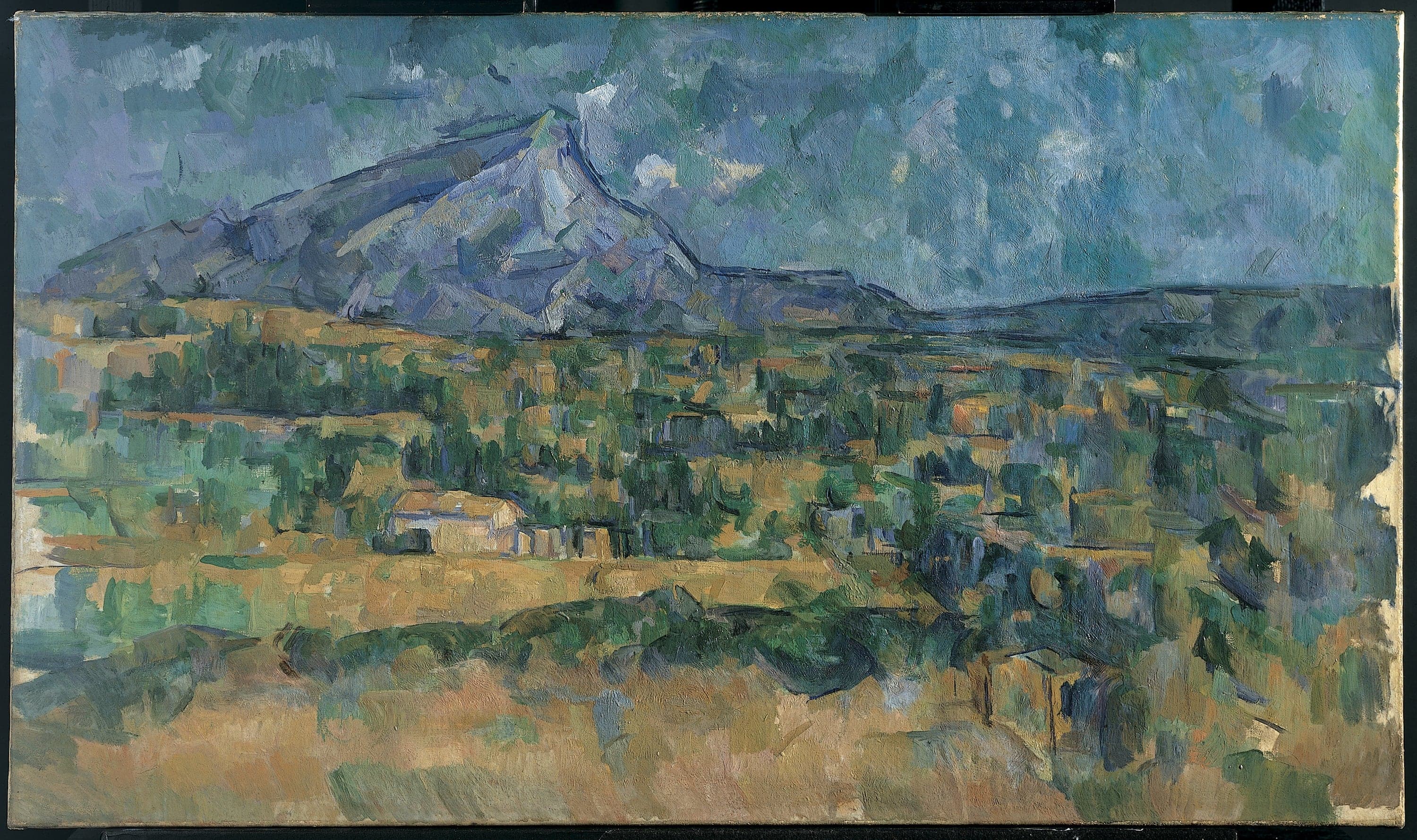 A wide, low landscape. A pale grey-blue limestone ridge runs across the upper third of the canvas, with a long shallow slope to the left and a steeper fall to the right. Below it a plain is built from small rectangular strokes of green, ochre, rust and blue laid side by side without blending, a few reading as roofs among trees. The sky is worked in the same patchwork in cooler colours