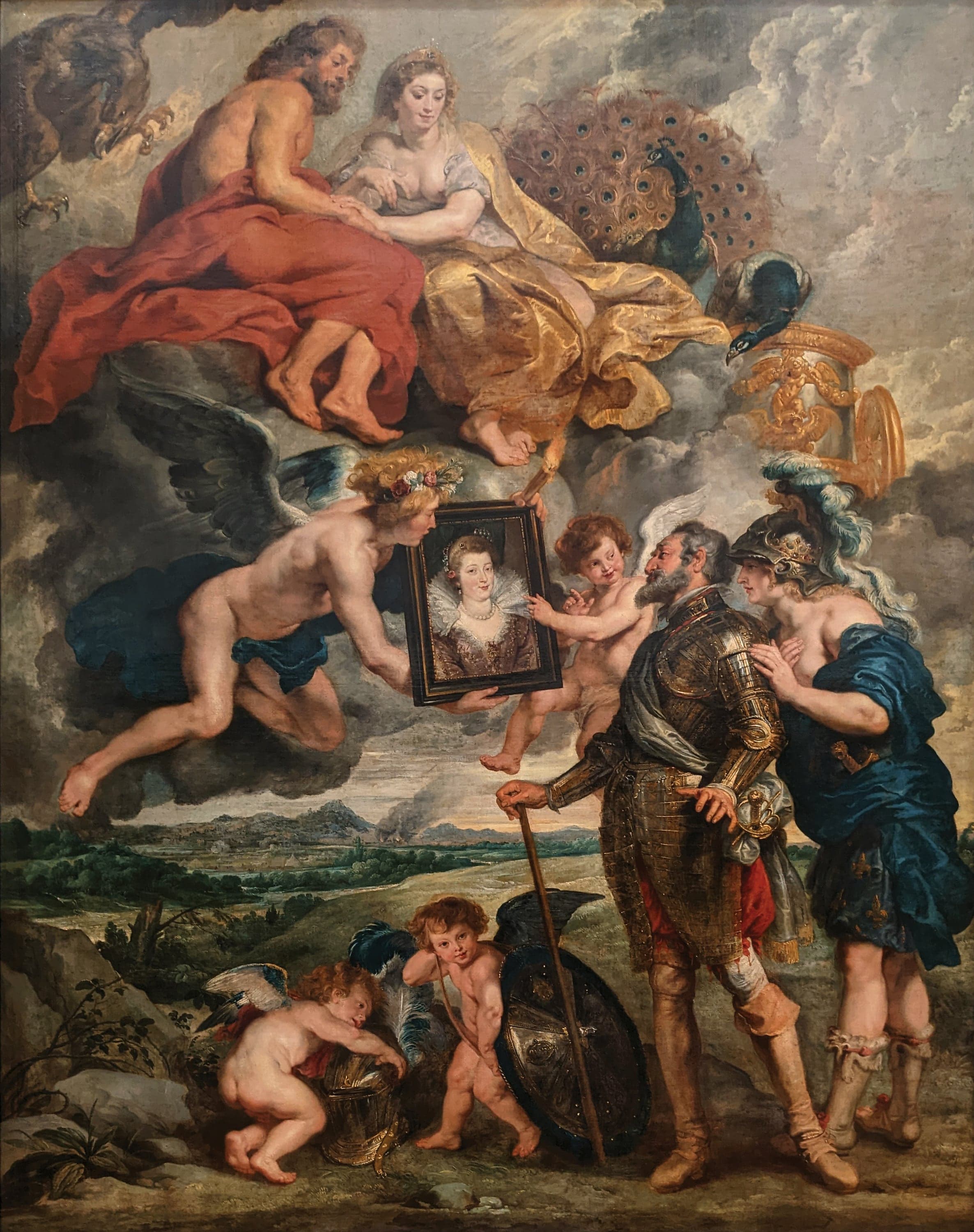 A tall canvas. At the right a bald, grey-bearded man in gold-chased armor and a red sash leans on a long staff and looks at a small portrait of a woman in a lace collar, held up in a black frame by a winged youth with flowers in his hair. A red-haired winged child points at the portrait. Behind the man stands a helmeted woman in a blue cloak covered in gold fleurs-de-lis with a hand on his shoulder. Above, on clouds, a bearded man wrapped in red sits beside a woman in gold whose peacock spreads its tail. An eagle hangs in the top left corner and a gilded chariot stands at the right. At the bottom two winged children play with a helmet and a large shield in front of a flat green landscape with distant smoke