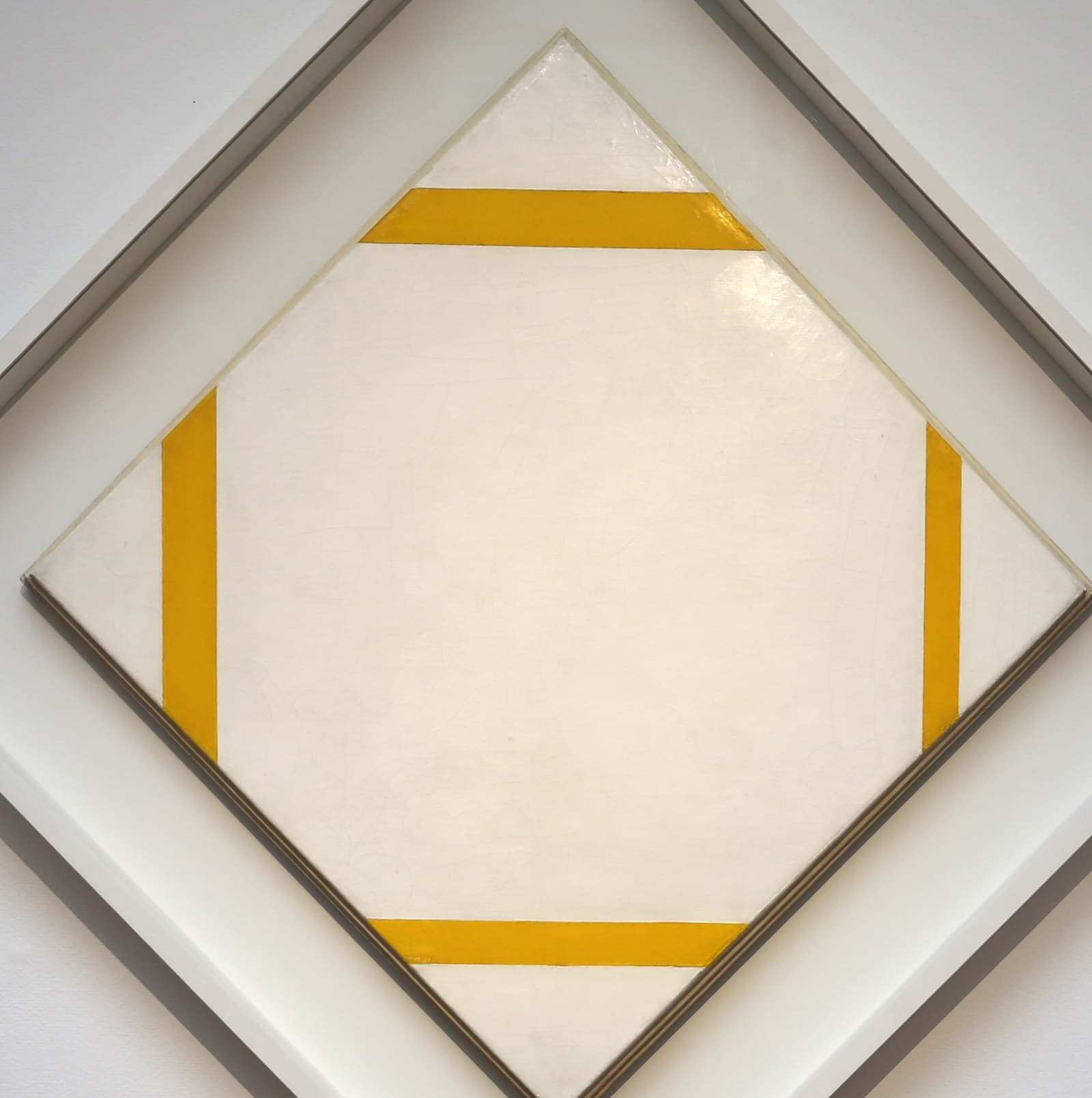 A square canvas hung on its corner as a diamond, painted off-white, with four deep yellow lines. Two run horizontally near the top and bottom points and two vertically near the left and right points, each crossing from one canvas edge to another and cutting a triangle off a corner. None of the lines touches another, and there is no black anywhere. The canvas sits in a narrow stepped dark moulding inside a white box frame