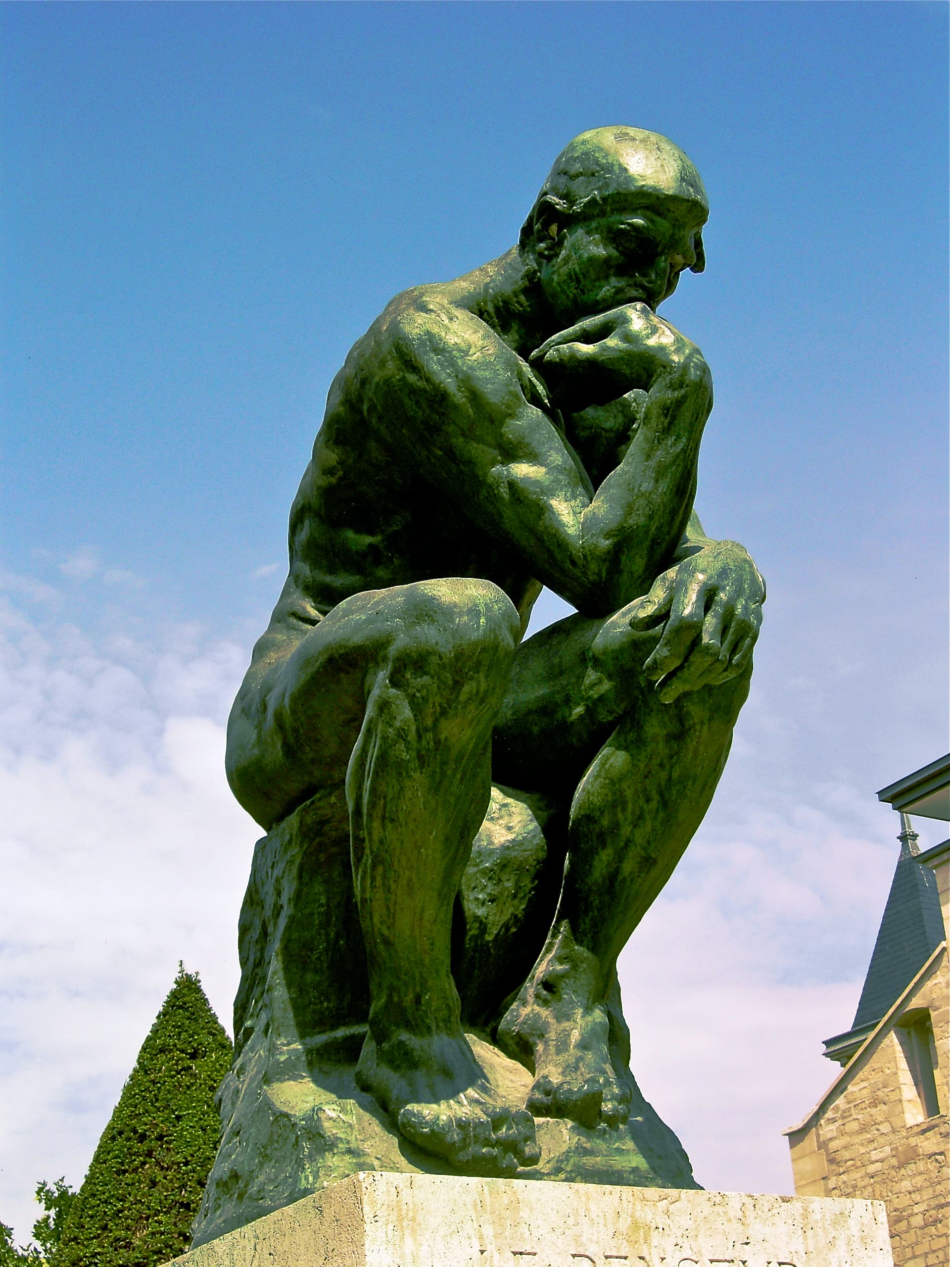 Auguste Rodin's monumental bronze Thinker in the Musée Rodin garden: a nude man seated on a rock, leaning forward with his chin against his right hand