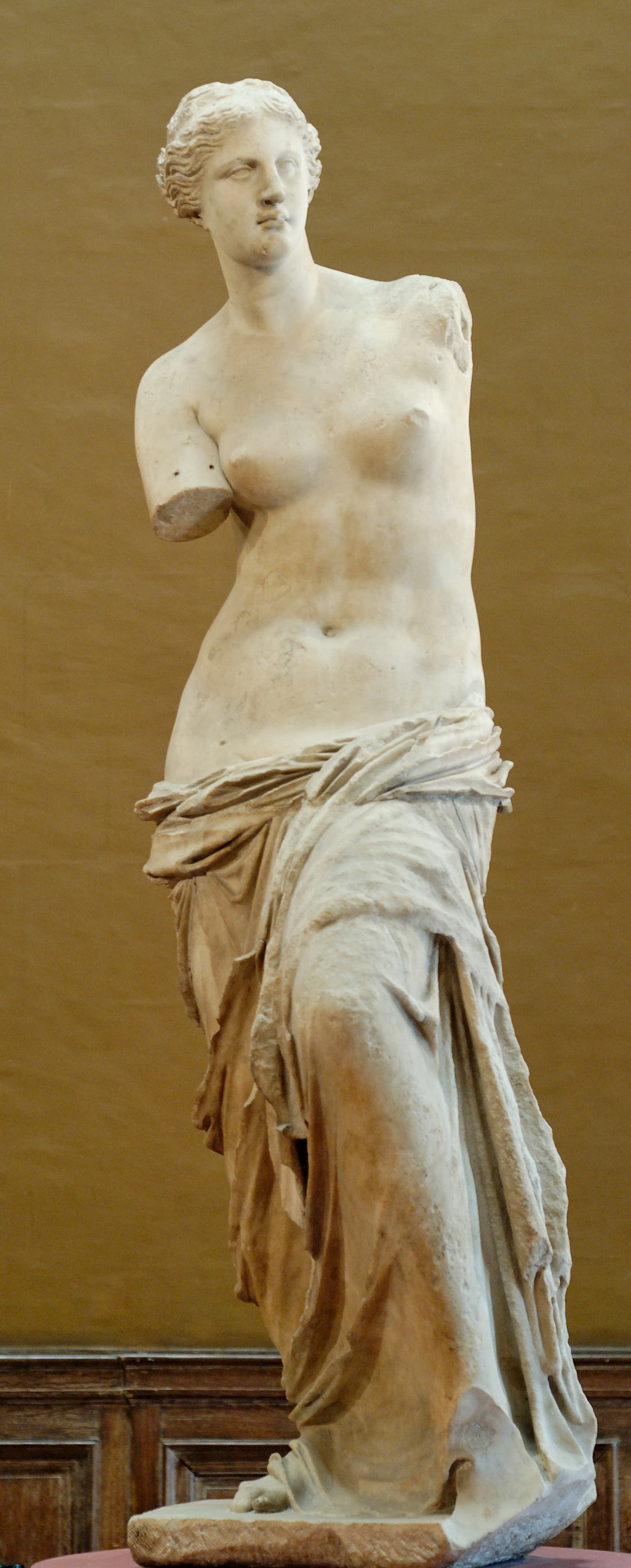 The Venus de Milo in the Louvre: a larger-than-life marble figure of Aphrodite, bare to the waist with drapery gathered around her hips and both arms missing
