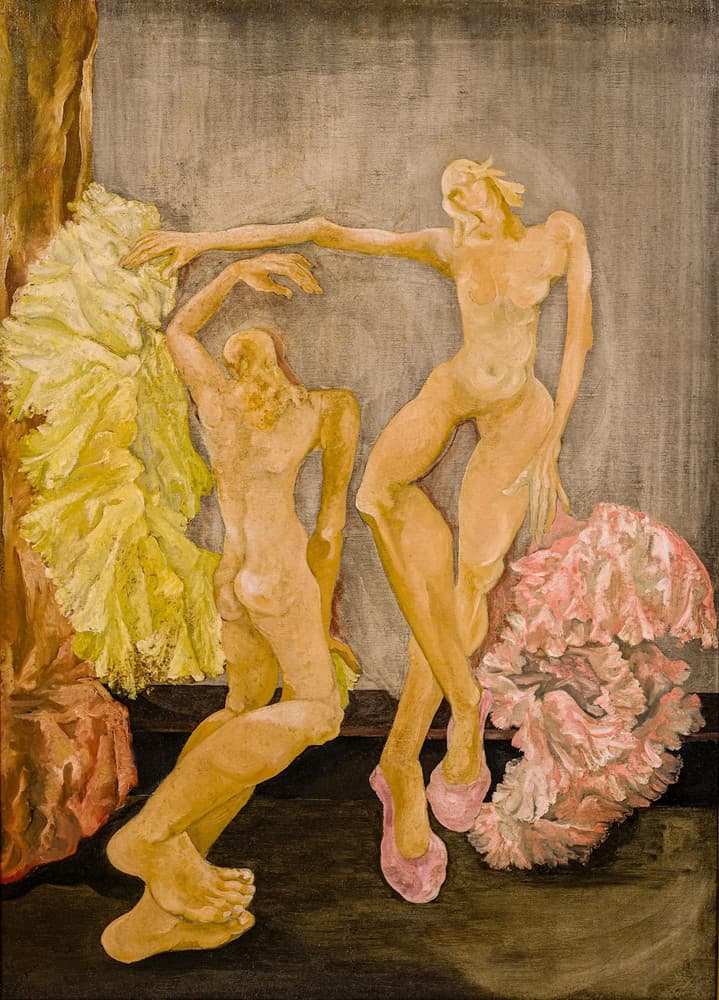 Two nude dancers painted in orange-tan against a grey wall. The one on the right stands on one leg in pink ballet slippers, head thrown back, one arm stretched out to the left; the one on the left sits on the floor with her back turned, one arm raised so that their hands meet at the top, her legs stretched to the lower left and ending in an enormous foot. A yellow-green ruffled tutu hangs at the left before a red-orange curtain, and a pink tutu lies on the floor at the right