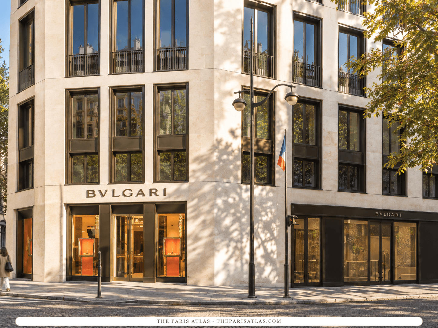 Reference-based illustration of the corner of the Bvlgari Hotel Paris building: pale stone walls with tall bronze-framed windows, the word BVLGARI above a ground-floor shop, a street lamp and a French flag.