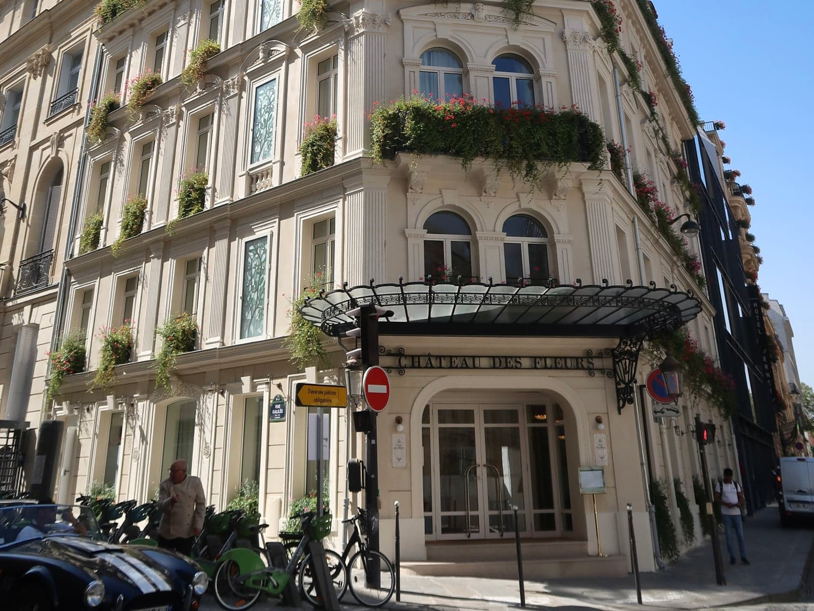 Photograph of Hôtel Château des Fleurs at the corner of rue Vernet and rue Galilée: a pale stone corner building with flower-filled balconies, stained-glass windows, a glass-and-iron canopy and the words Château des Fleurs above the glazed entrance doors.