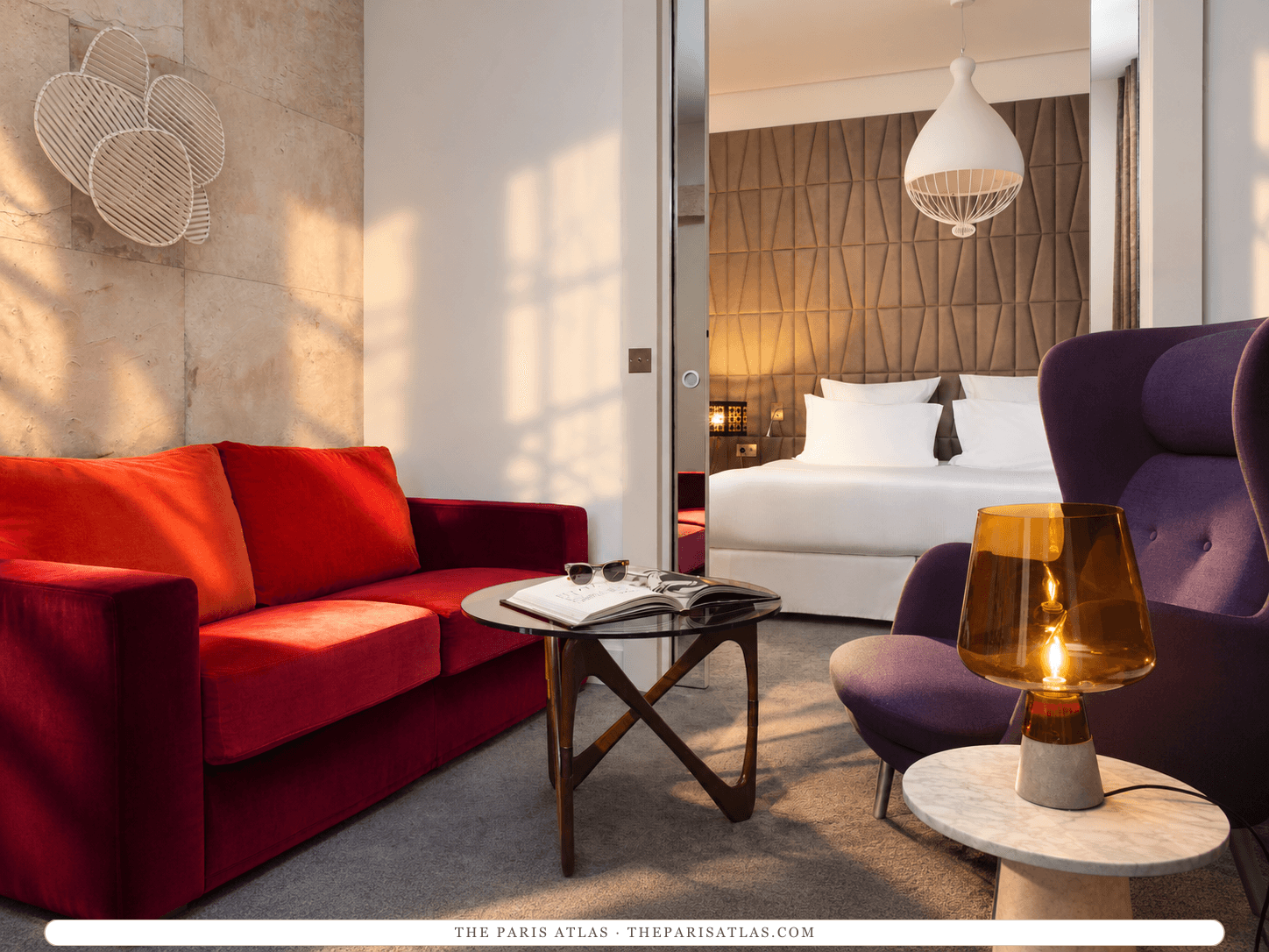 AI-generated illustration of a suite at Hôtel Dupond-Smith: a red velvet sofa and a purple armchair around a low glass table in the sitting area, with a white bed beyond a partition.
