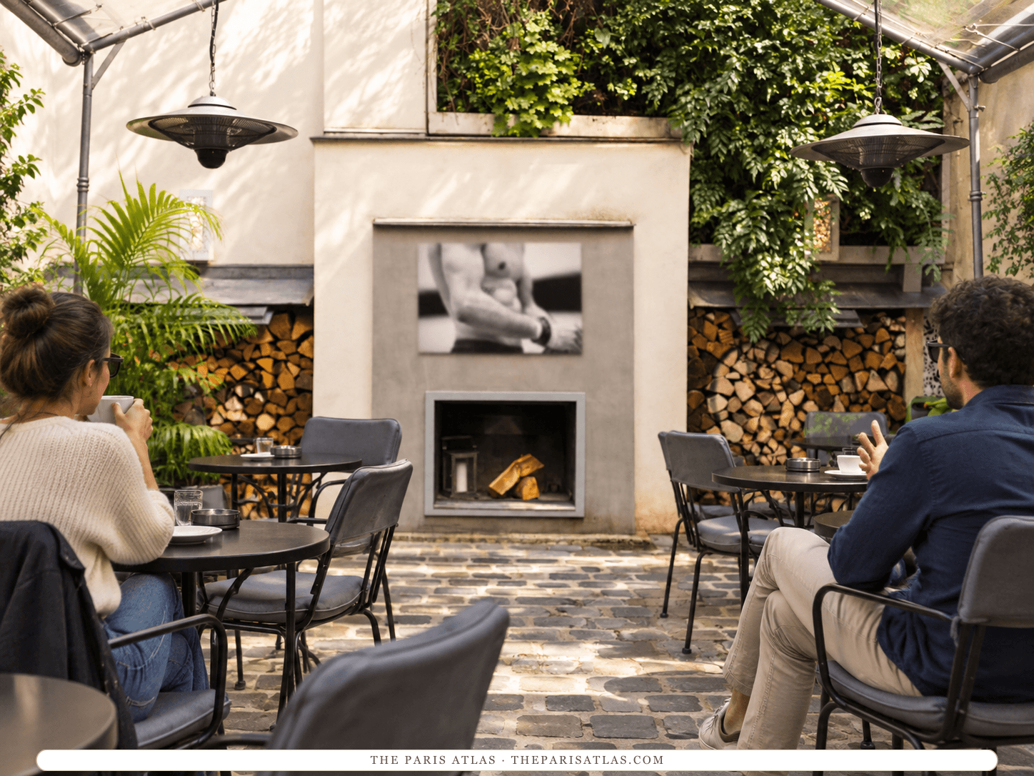 Reference-based illustration of the courtyard terrace at Hôtel Jules & Jim: guests at small tables on cobbles, an outdoor fireplace set in a white wall with a black-and-white photograph above it, stacked logs, hanging heaters and climbing plants.