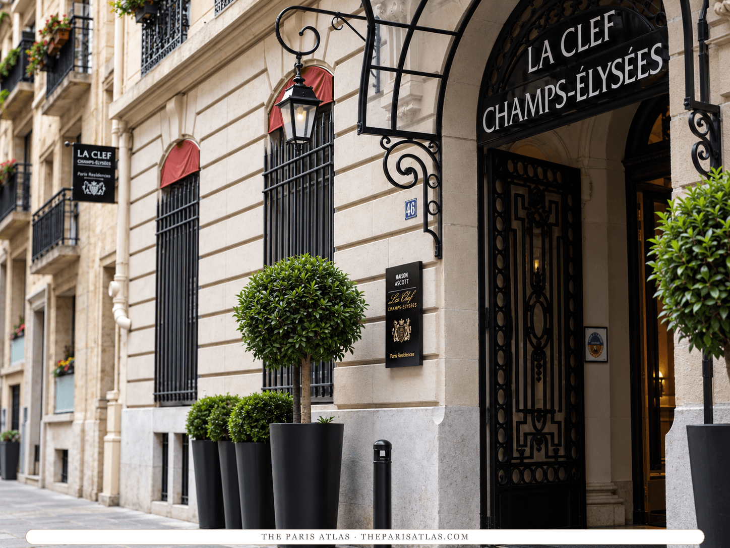 AI-generated illustration of the entrance to La Clef Champs-Élysées on rue de Bassano: a carved stone archway with black wrought-iron doors, the hotel's name above the arch, red window awnings and clipped trees in black planters.
