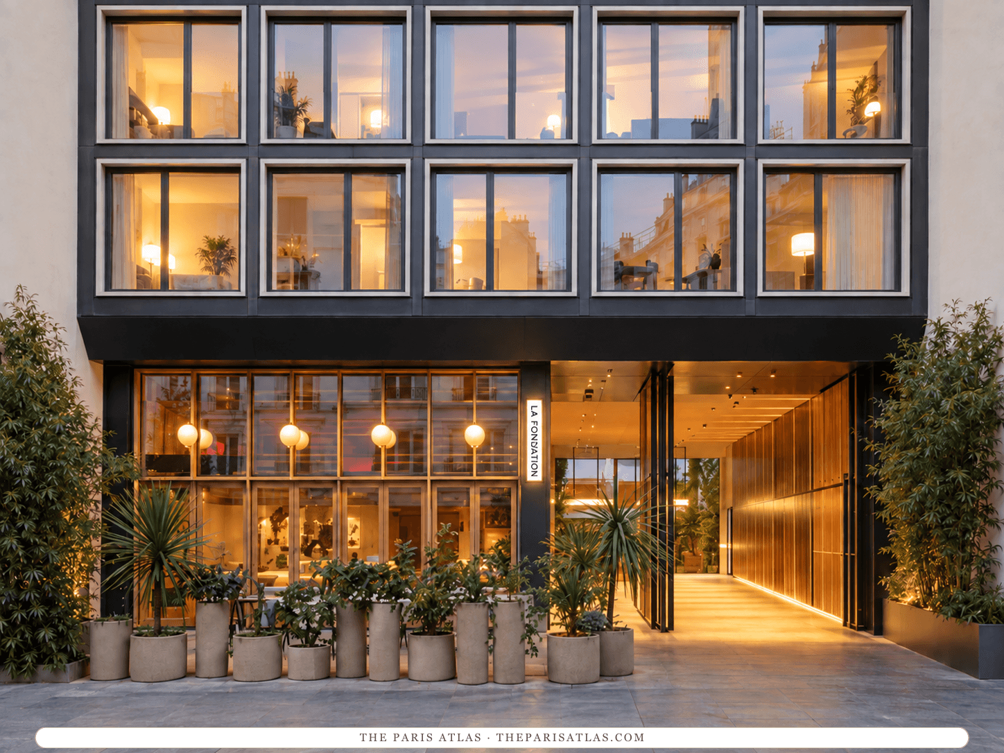 AI-generated illustration of La Fondation on rue Legendre: a façade gridded in dark metal around large lit windows, a glazed ground floor with potted plants, and a warm-lit passage leading into the building.