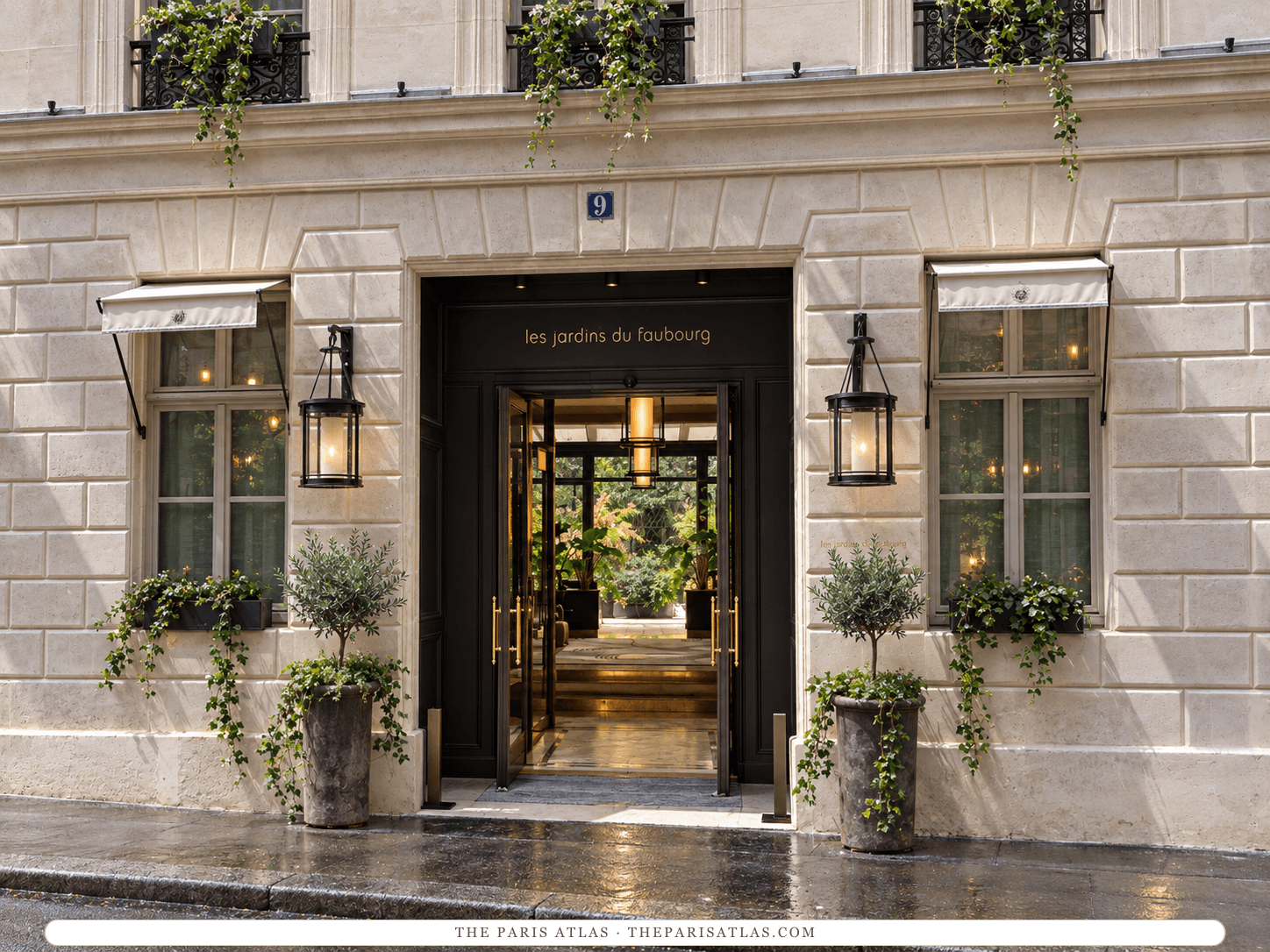 AI-generated illustration of the entrance to Les Jardins du Faubourg at 9 rue d'Aguesseau: a dark doorway with the hotel's name in small lowercase letters, cylindrical lanterns, white awnings, potted trees and trailing plants on a wet pavement.