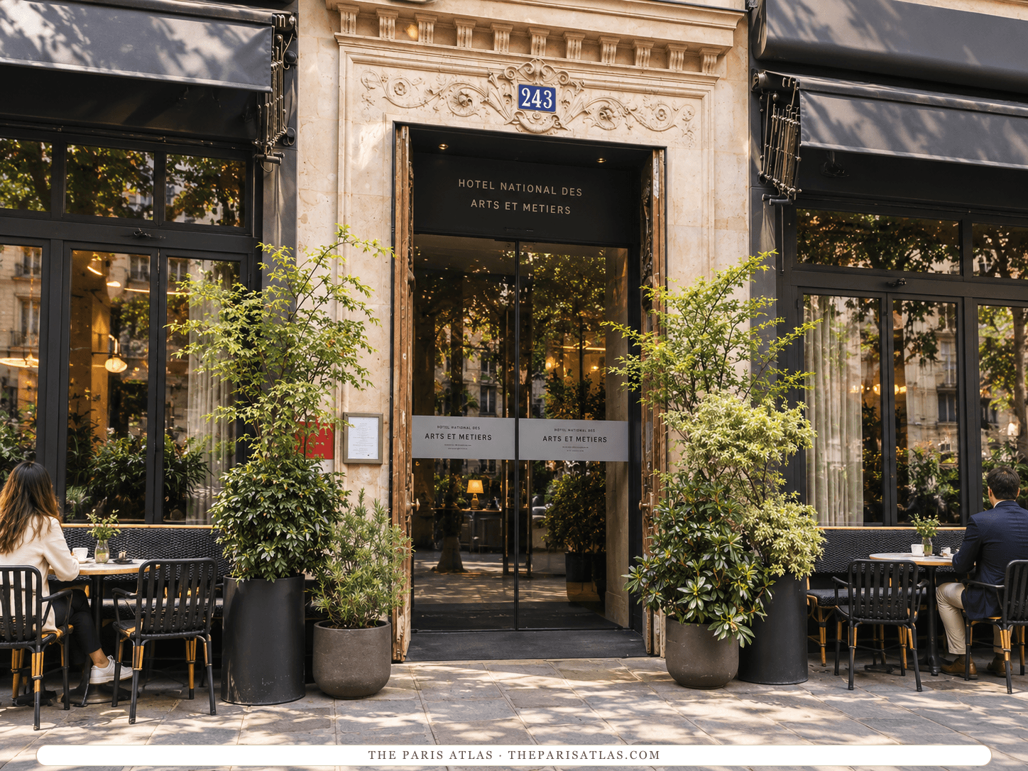 Reference-based illustration of the entrance of Hôtel National des Arts et Métiers: a carved stone portal with a blue number 243 plaque over glass doors, potted trees, dark awnings and café tables on either side.