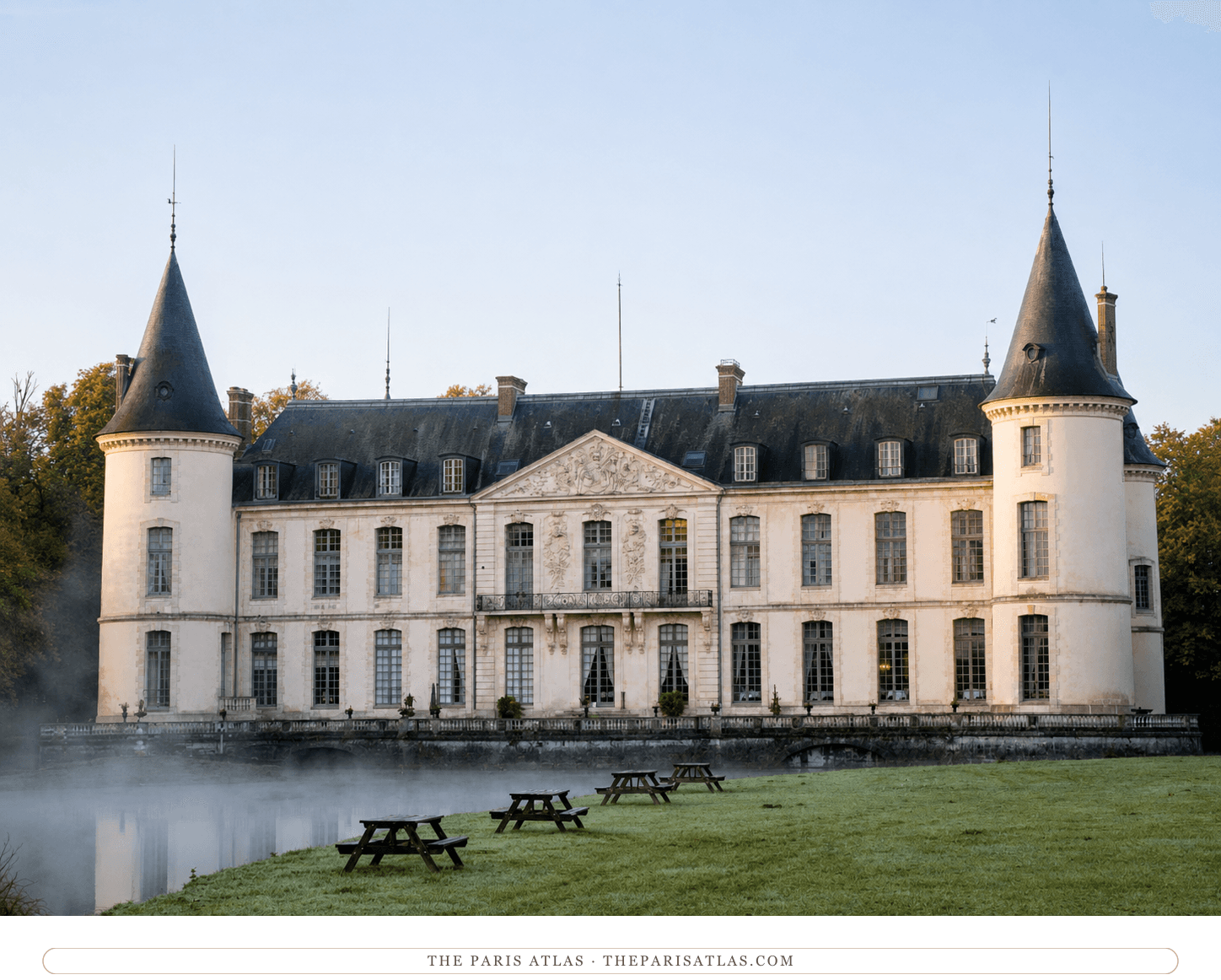 The same château in colour, pale stone and slate towers above the mist on the moat at dawn