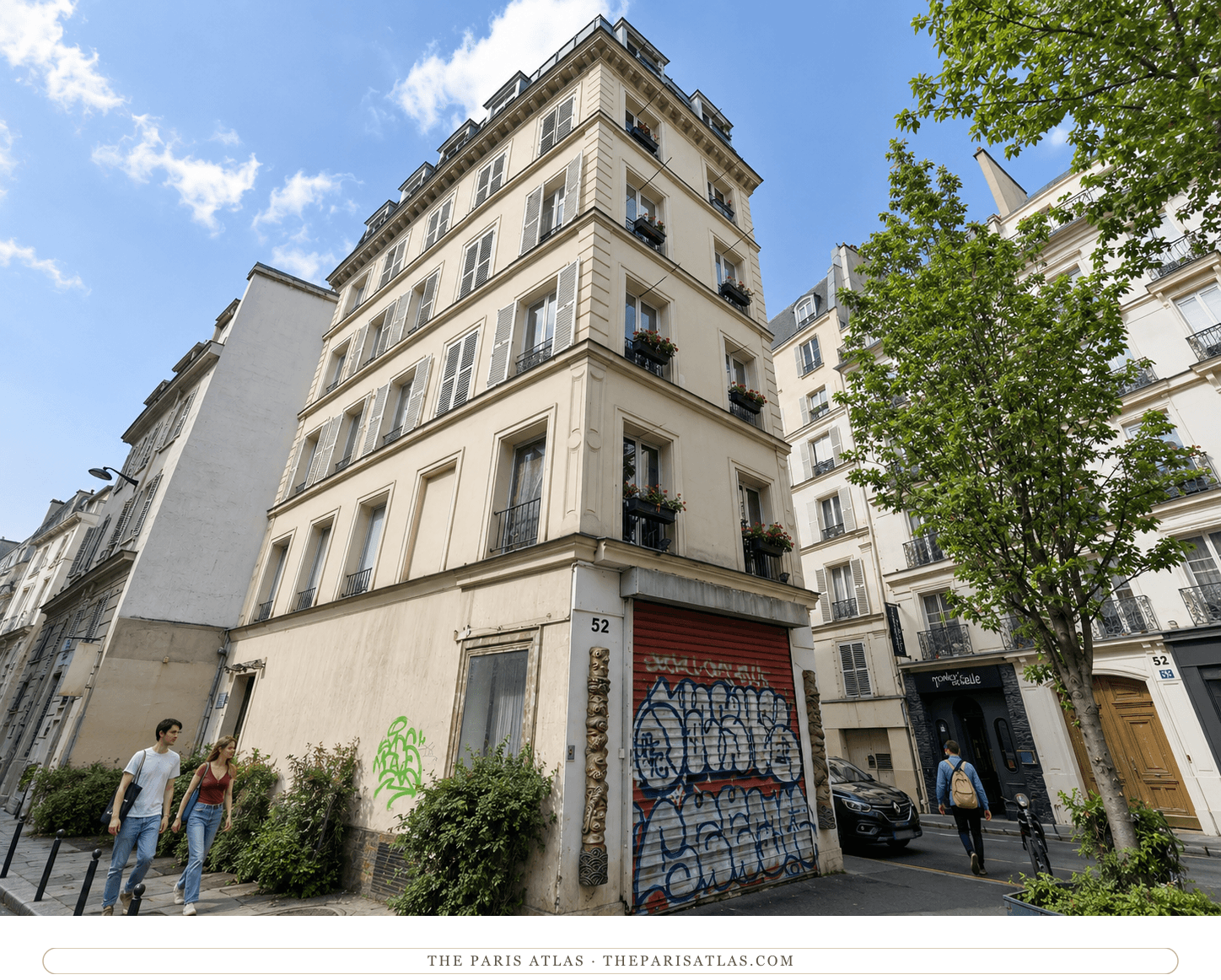 The same corner at 52 rue Jean-Baptiste Pigalle in color, cream facade under a blue sky, red shutter tagged with graffiti