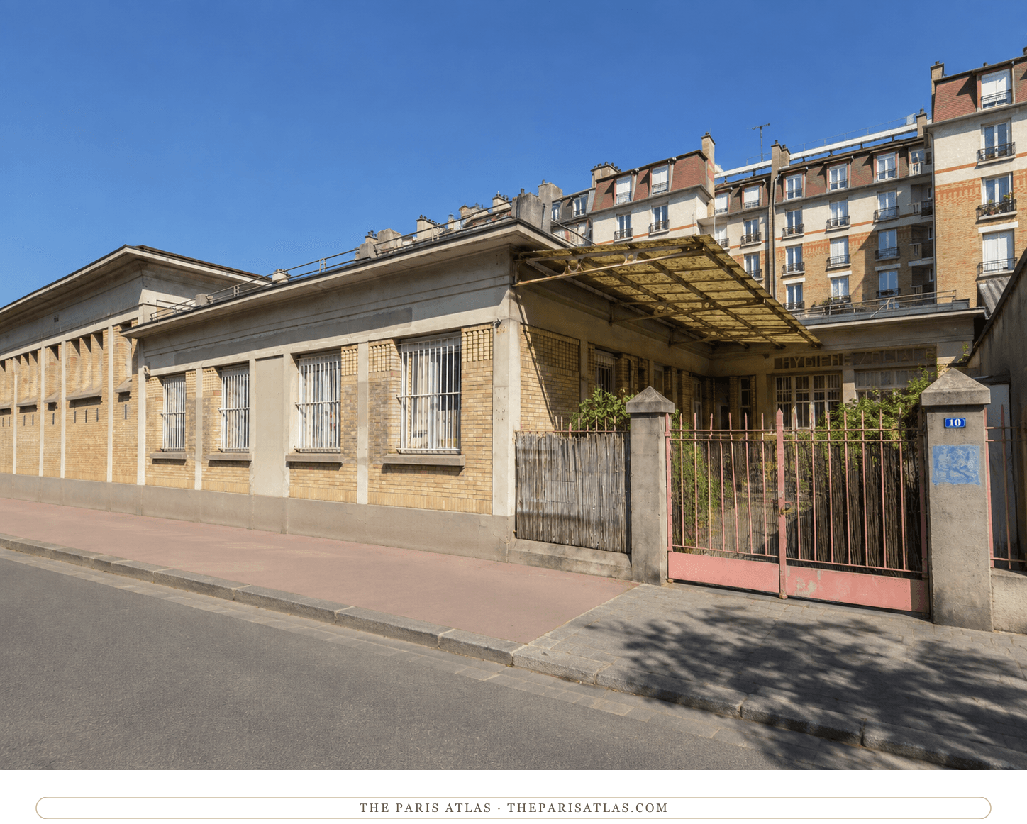 Present-day color view of the surviving low brick dispensary building at 10 rue Fanny under a clear blue sky, with its projecting canopy, red gate and number 10 gatepost