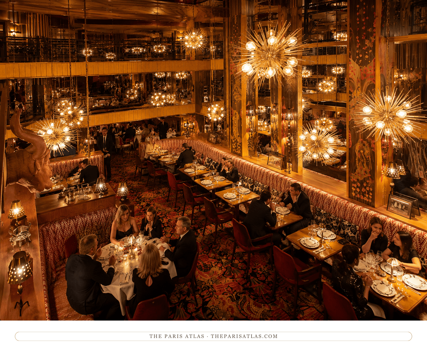 The rue du Colisée dining room of Le Bœuf sur le Toit today, starburst chandeliers and a bull's head over patterned banquettes