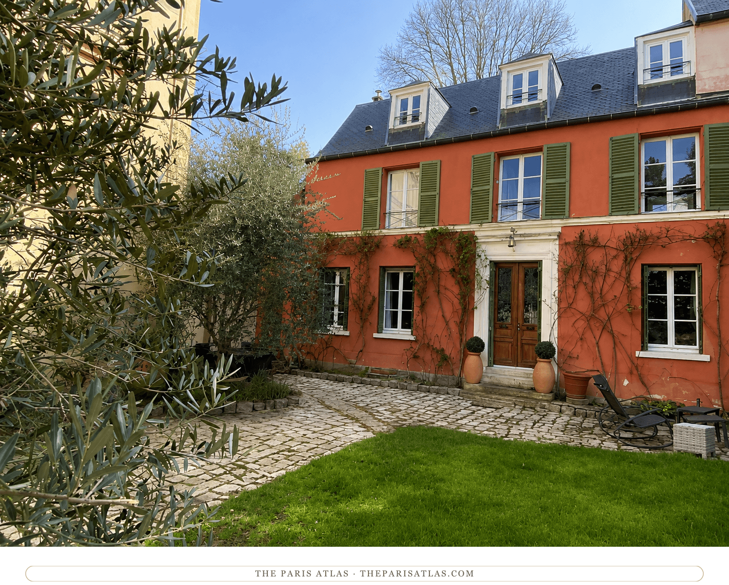 The Louveciennes house in color — salmon-pink walls, green shutters, vines climbing around the wooden door, lawn and cobbles in the courtyard.