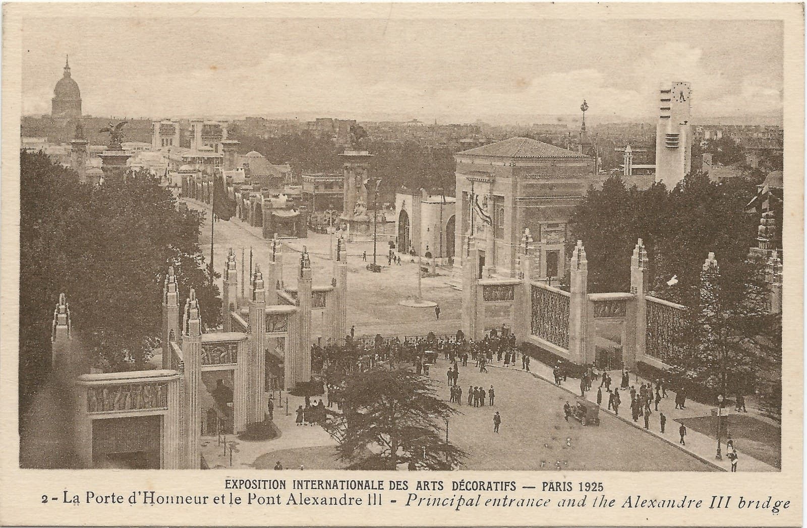 Aerial view of the 1925 Paris decorative arts exhibition: tall square pylons flanking the Porte d'Honneur entrance, crowds on the paths below, pavilions and a clock tower spreading toward the Invalides dome