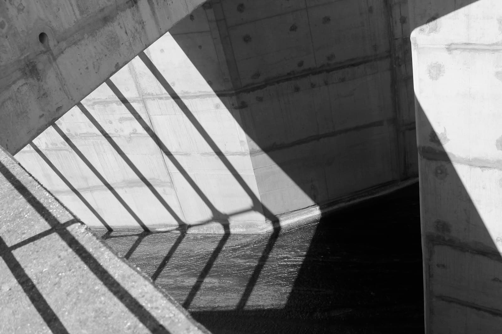 Sunlight through a railing breaking into diagonal planes of shadow across bare concrete