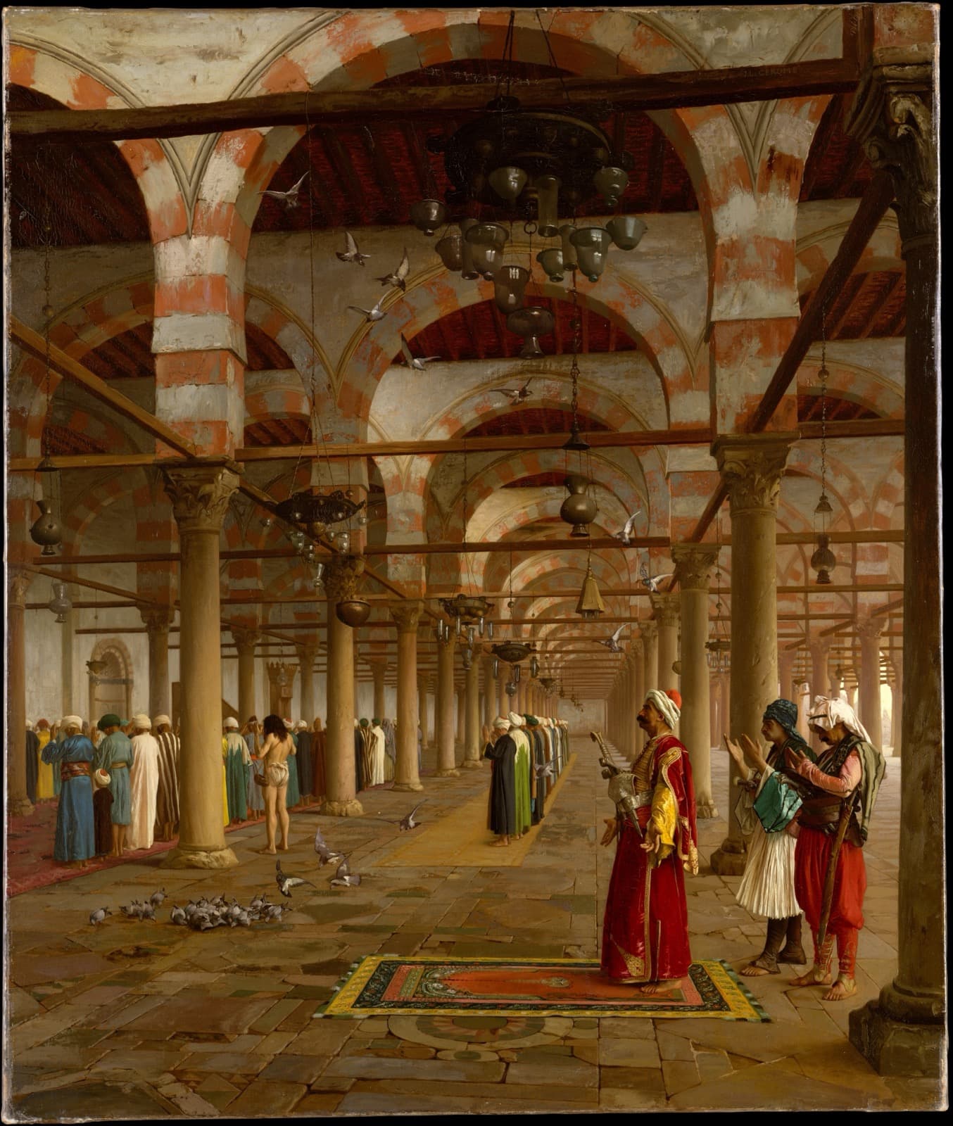 A large mosque interior painted in fine detail: rows of slender columns supporting red-and-white striped arches, brass lamps hanging on long chains, pigeons on the stone floor. Worshippers in pale robes stand in rows along the left. In the right foreground a group of men in red, white and striped dress stand with hands raised in prayer, one on a patterned rug laid across the flagstones.