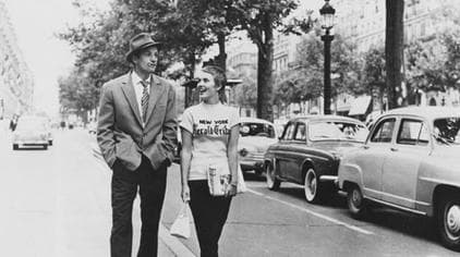 Jean-Paul Belmondo in a fedora and Jean Seberg in a New York Herald Tribune T-shirt walking along the Champs-Élysées, parked 1950s cars at the curb