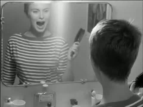 Jean Seberg laughing in a bathroom mirror, striped shirt, with the back of Belmondo's head in the foreground