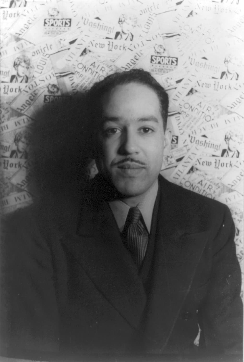 Studio portrait of Langston Hughes in 1936, in a suit and patterned tie, photographed against a patterned backdrop and looking past the camera