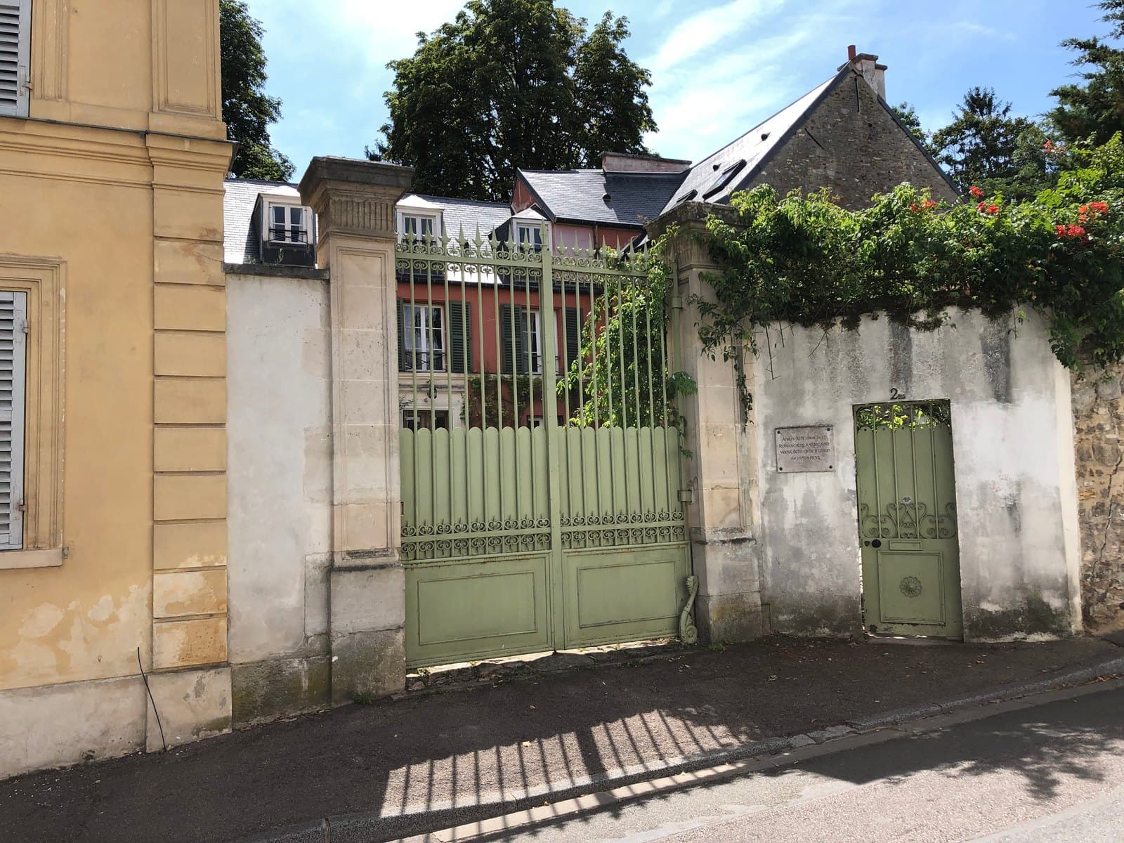 The green gates and street wall of 2 bis rue de Montbuisson in Louveciennes, the house where Anaïs Nin lived, with the commemorative plaque beside the pedestrian door