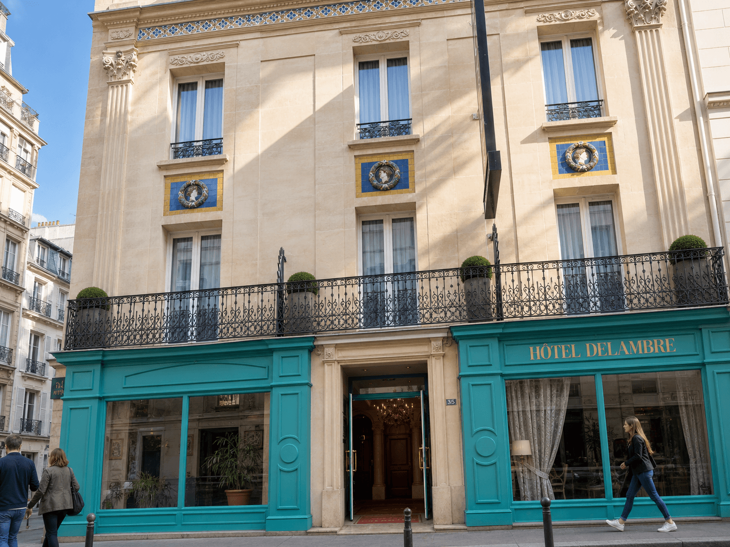 Photorealistic editorial illustration of Hôtel Delambre’s pale stone façade, turquoise storefront, and wrought-iron balcony in bright present-day daylight.