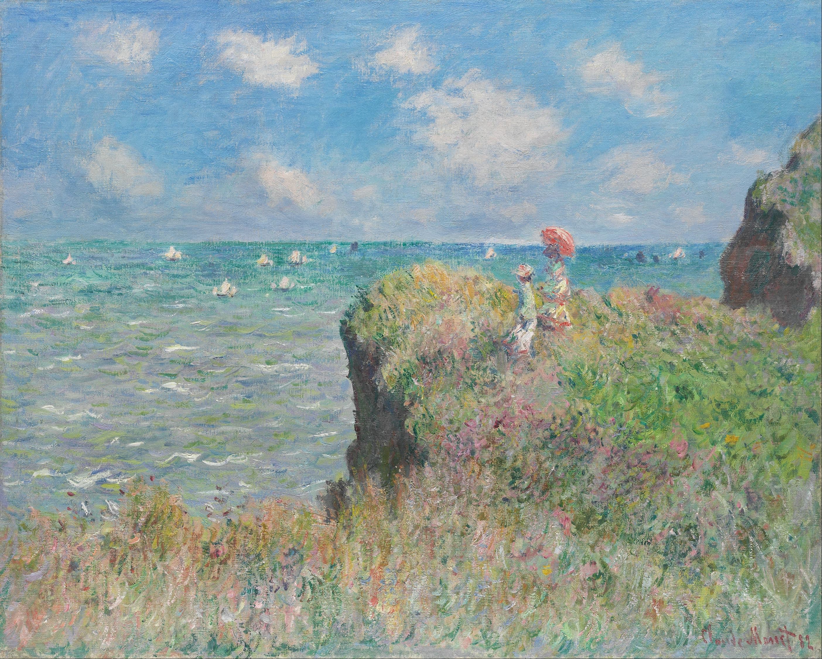 Close view of two women standing on the grassy cliff above Pourville, their dresses and veils moved by wind